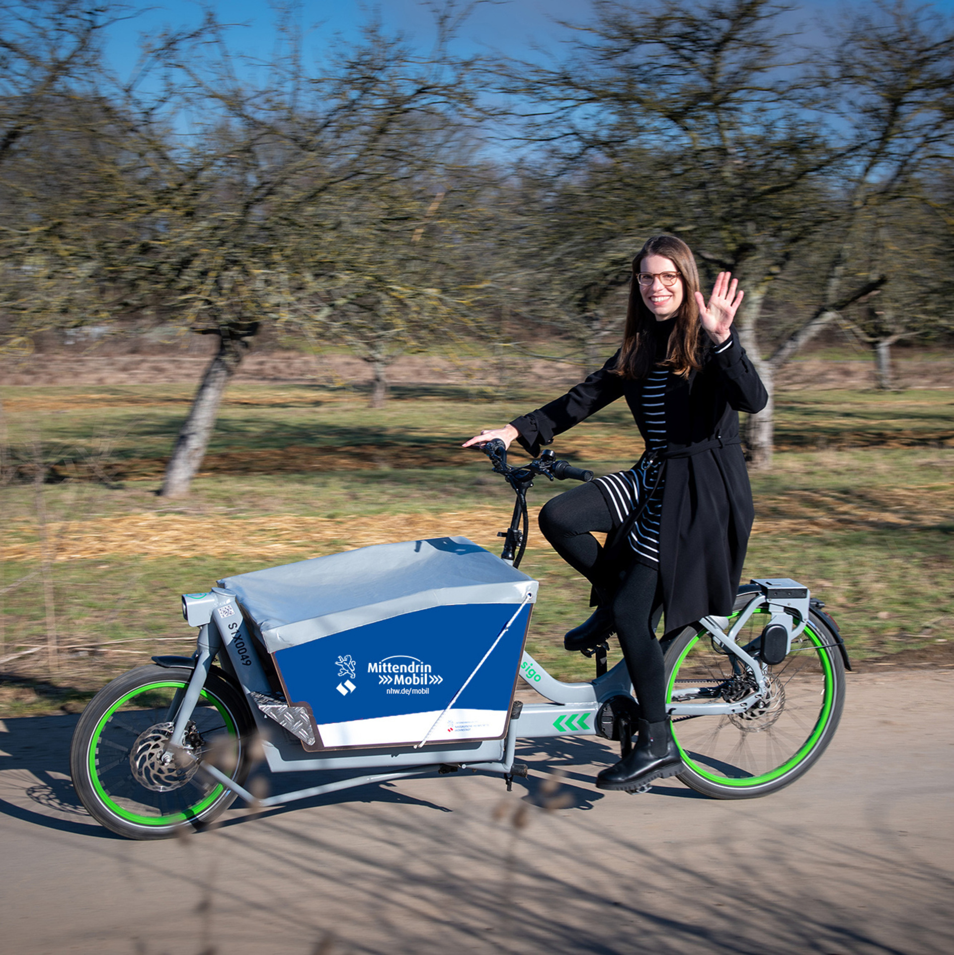 Frau fährt ein Lastenrad. Auf der Lastenradbox ist das NHW Logo und die URL nhw.de/mobil