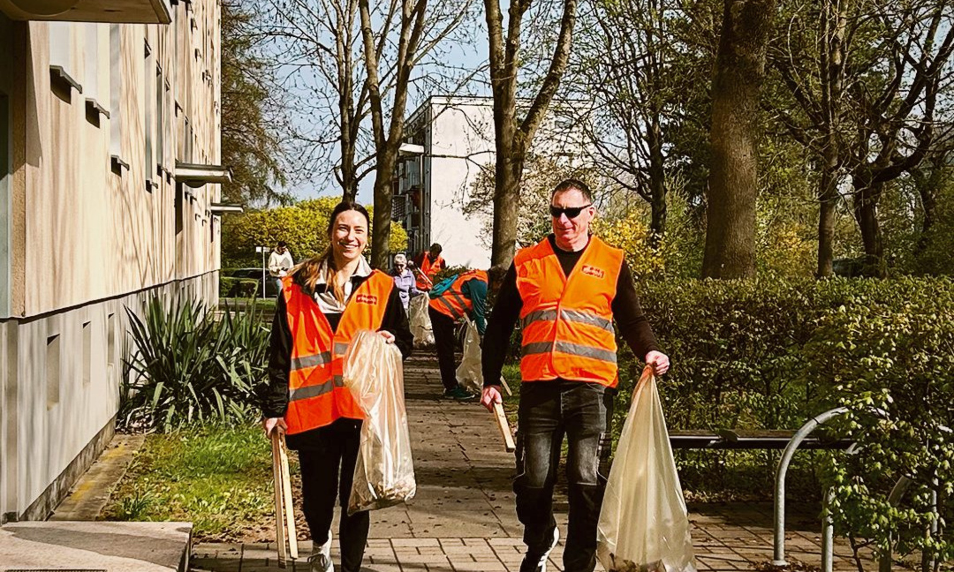 Zwei Erwachsenen in Warnwesten beim Müllsammeln.