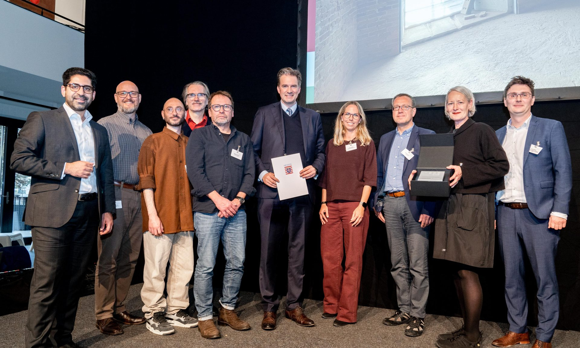 Große Bühne: Hessens Wohnungsbauminister Kaweh Mansoori (li.) übergibt den Hessischen Landespreis Baukultur 2025 für den Hochbunker Agathof im Beisein von Kassels Oberbürgermeister Sven Schoeller (Mi.) an Projektbeteiligte. 