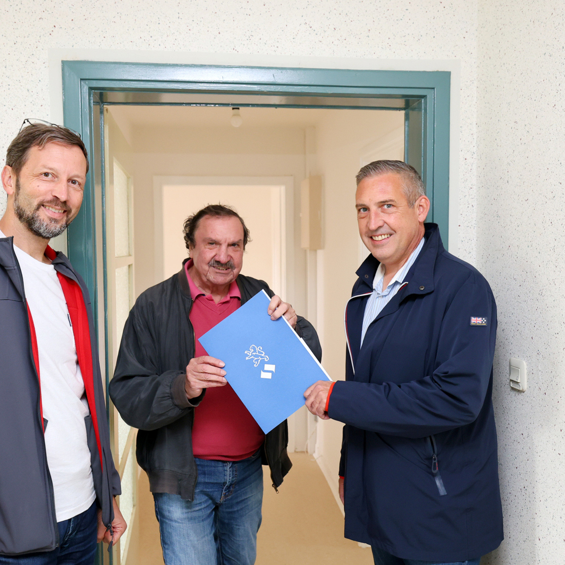 NHW-Regionalcenterleiter Sascha Holstein (re.) und Markus Beecht (li.), Geschäftsführer der Evangelischen Wohnraumhilfe, heißen Burgfried Göbel in seiner Wohnung willkommen.