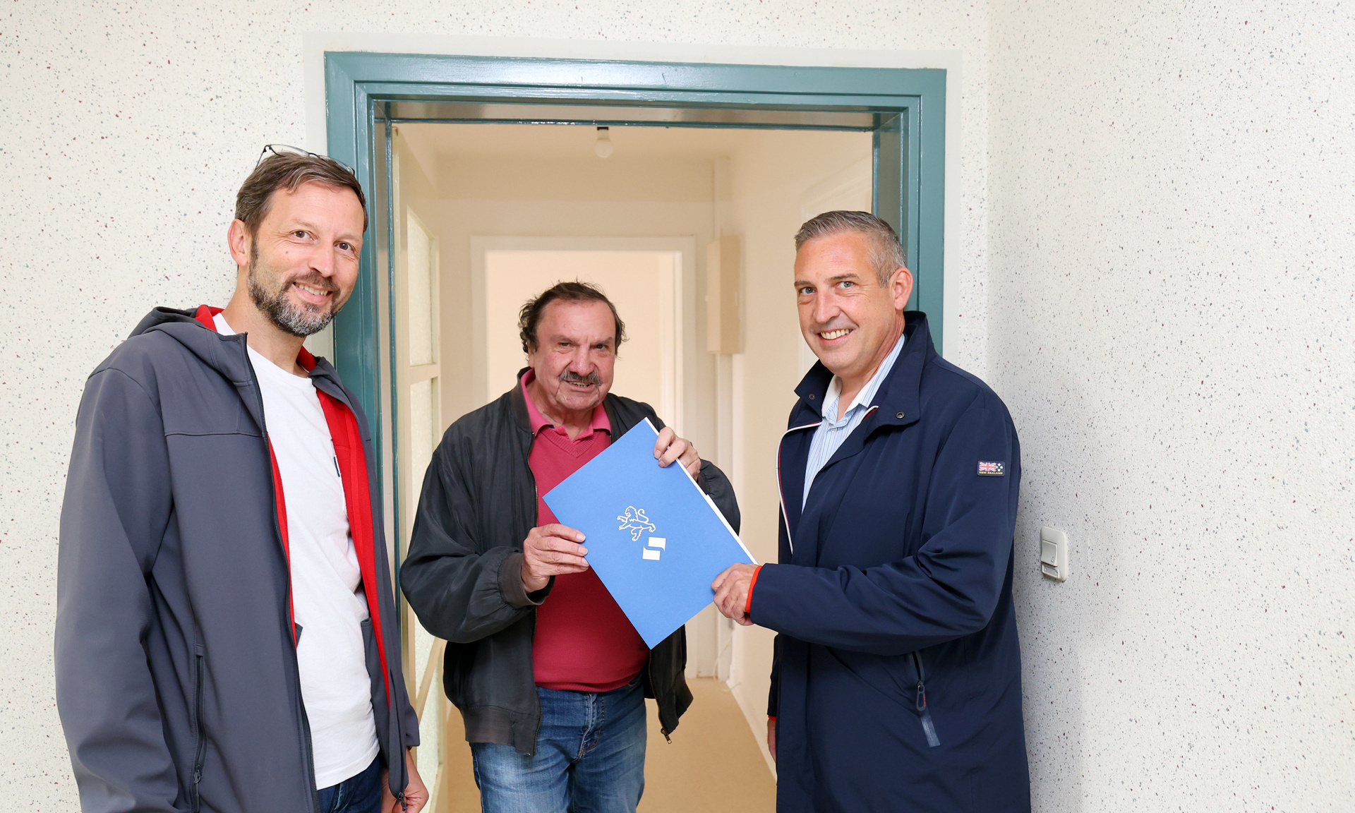 NHW-Regionalcenterleiter Sascha Holstein (re.) und Markus Beecht (li.), Geschäftsführer der Evangelischen Wohnraumhilfe, heißen Burgfried Göbel in seiner Wohnung willkommen.