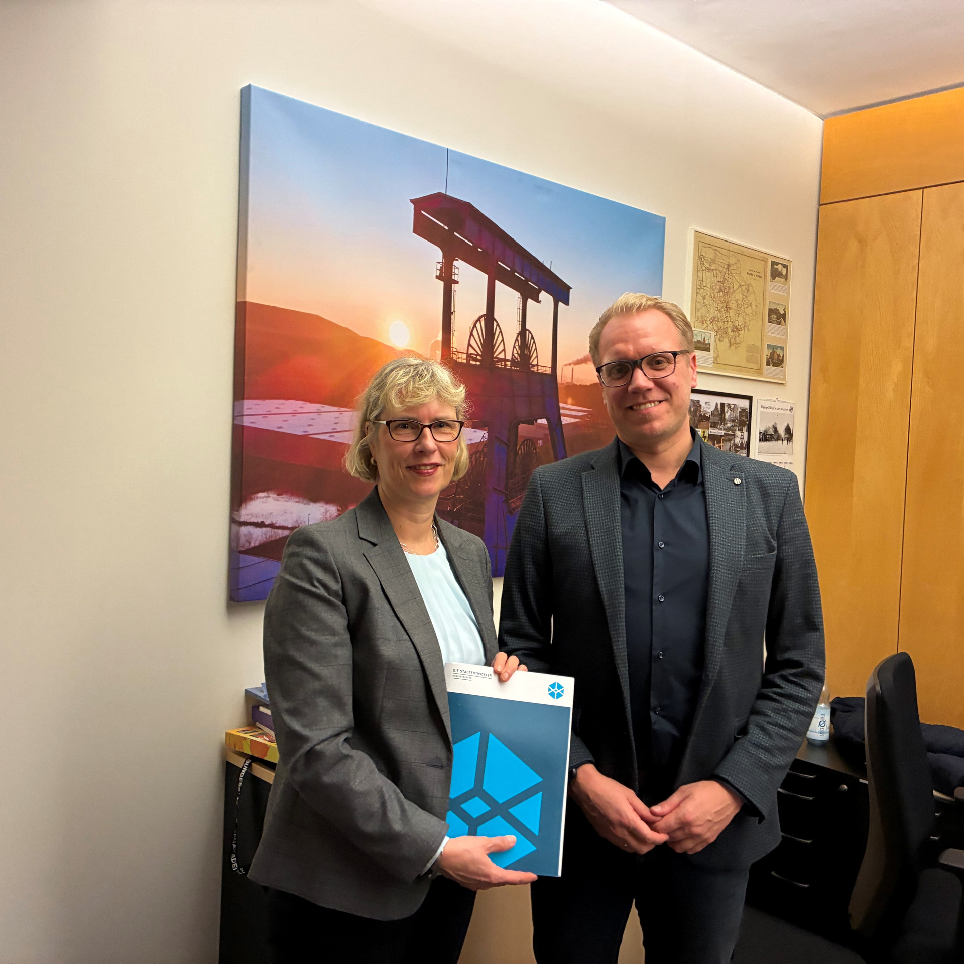 Monika Fontaine-Kretschmer und Hendrik Bollmann stehen mit dem Empfehlungspapier posierend der Kamera zugewandt.