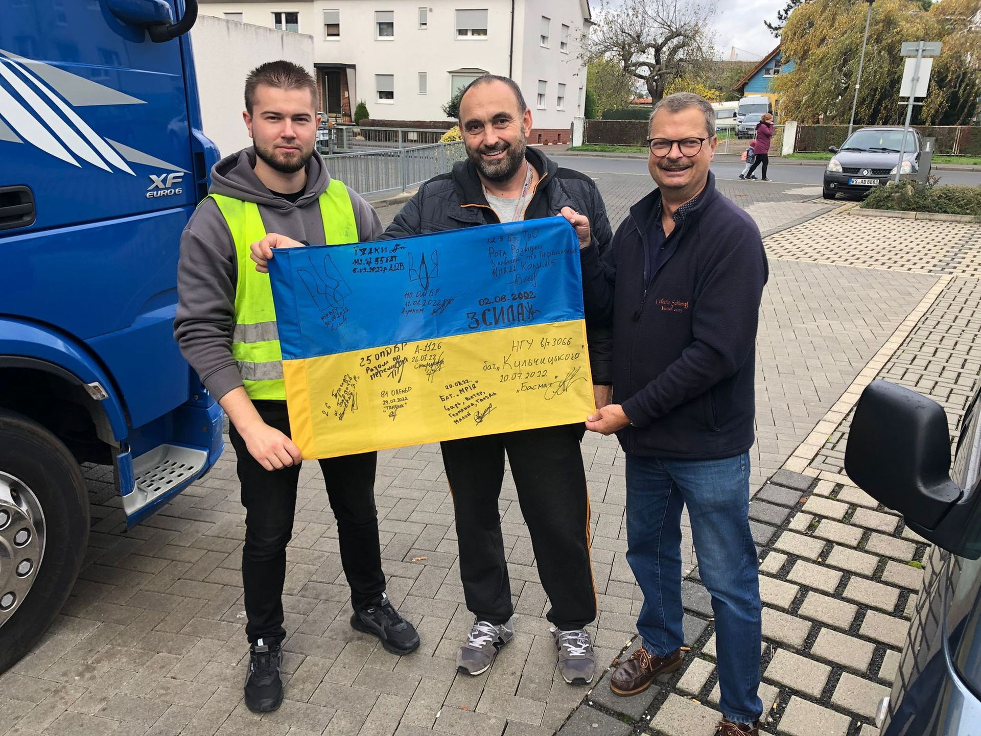 Drei Männer halten ein Plakat in den ukrainischen Farben hoch