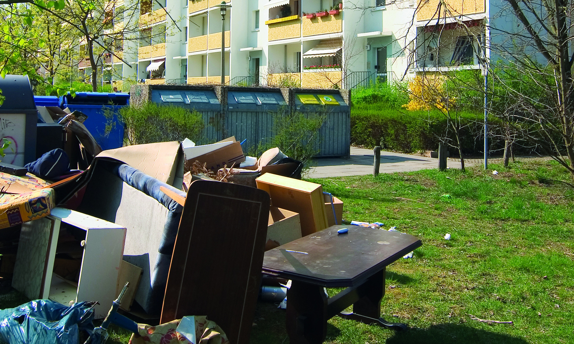 Zu sehen ist ein Stapel voller Sperrmüll auf einer Grünfläche vor einem Hochhaus.
