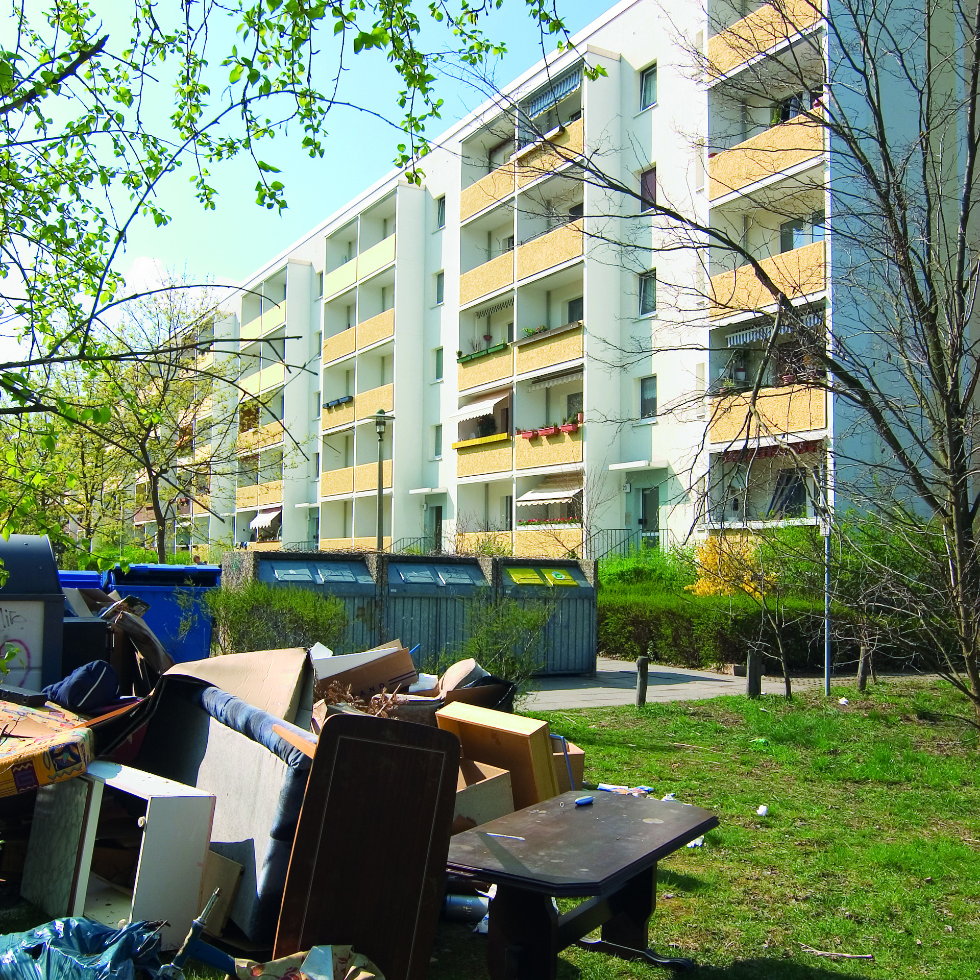 Zu sehen ist ein Stapel voller Sperrmüll auf einer Grünfläche vor einem Hochhaus.