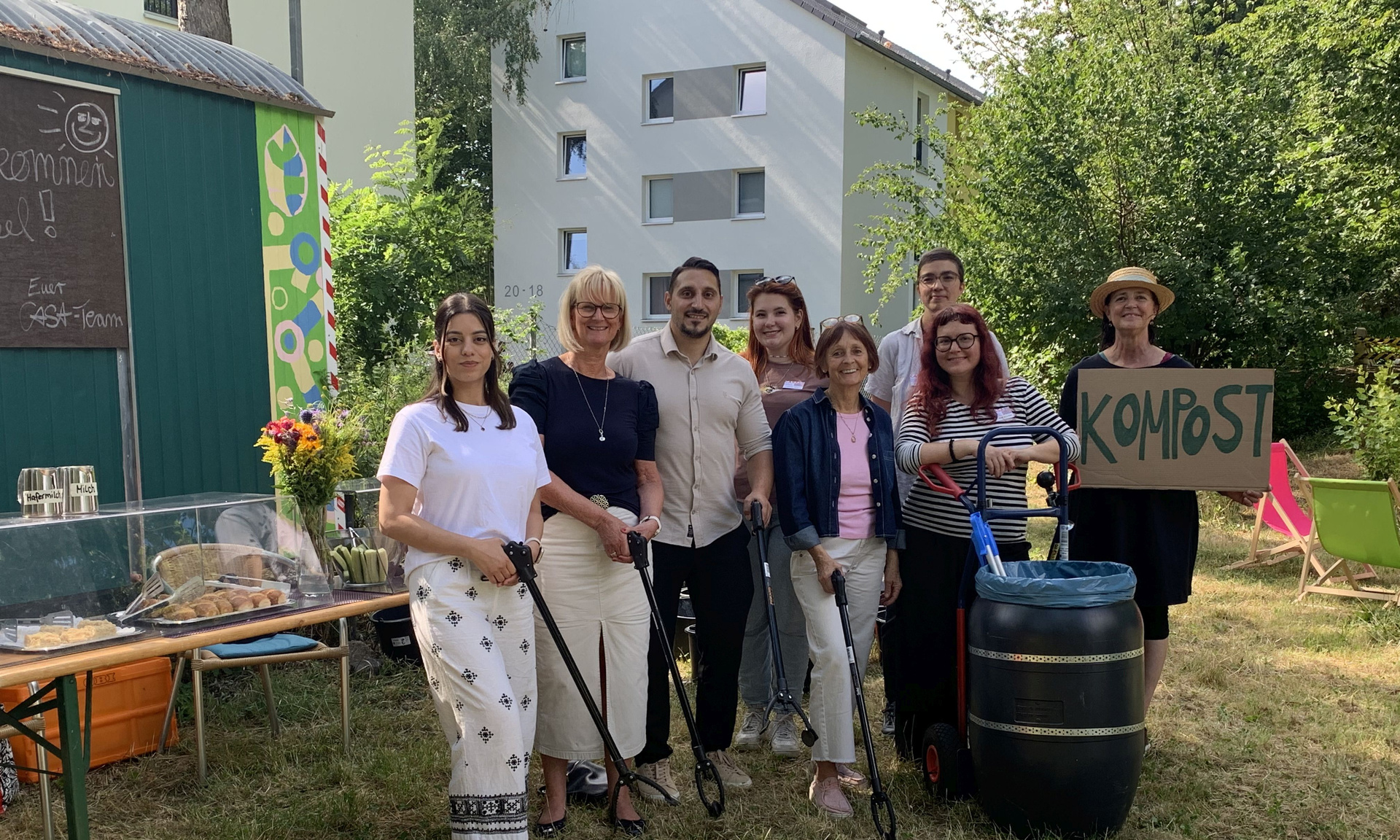 Gruppe von 6 Personen die zusammensteht und in die Kamera schauen. Eine Person hält ein Schild mit "Kostbar" hoch