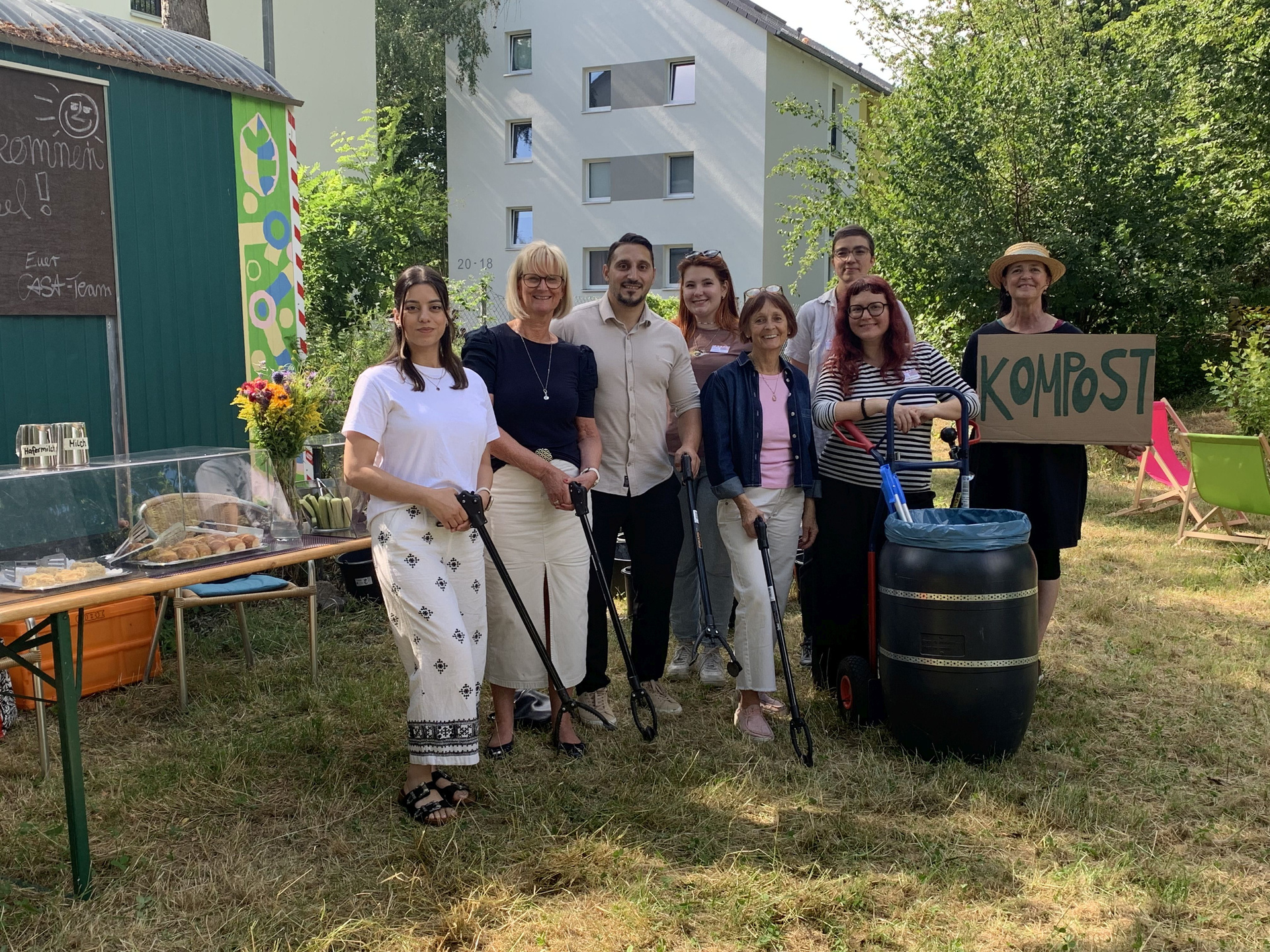 Gruppe von 6 Personen die zusammensteht und in die Kamera schauen. Eine Person hält ein Schild mit "Kostbar" hoch