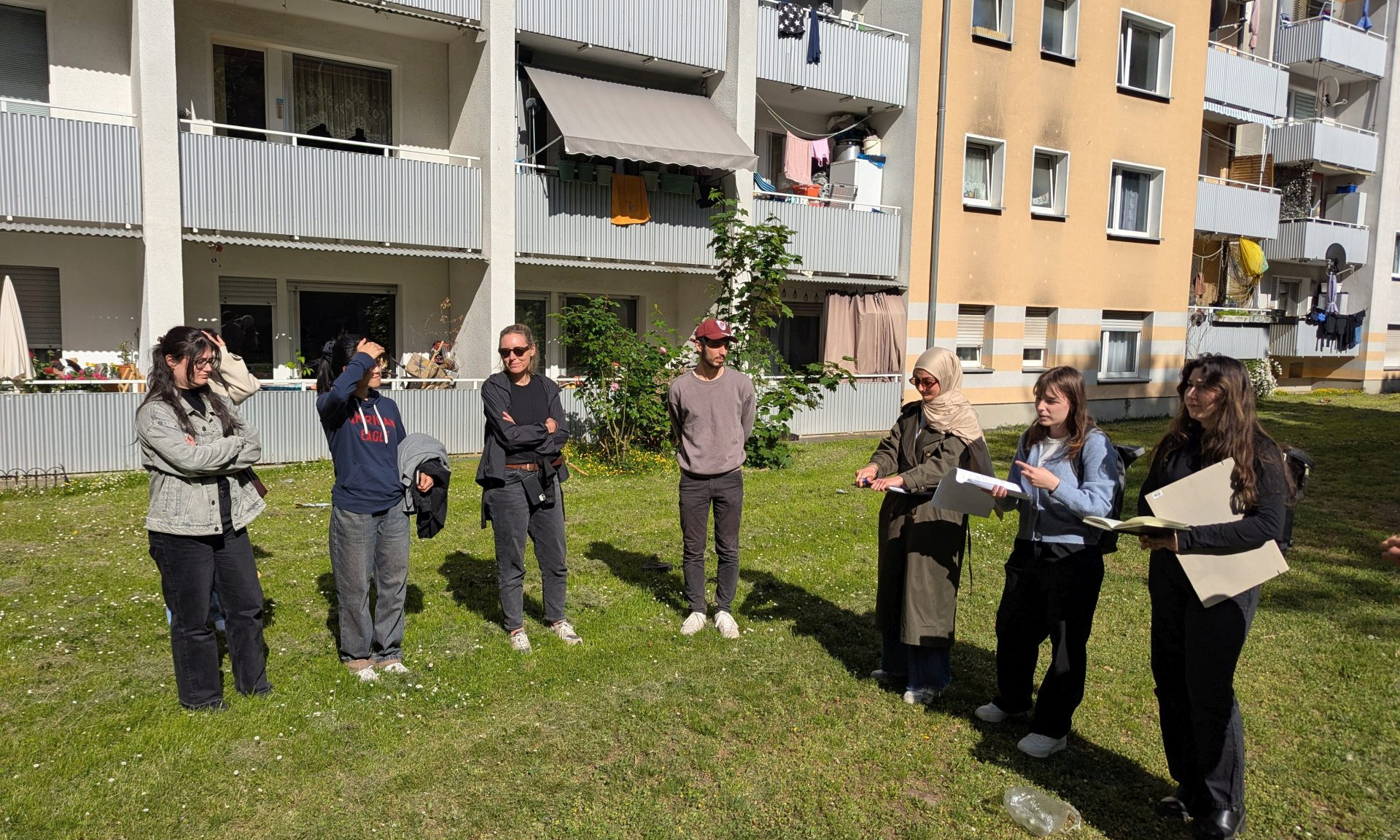 Mehrere Studierende auf einer Grünfläche vor einem Mehrfamilienhaus