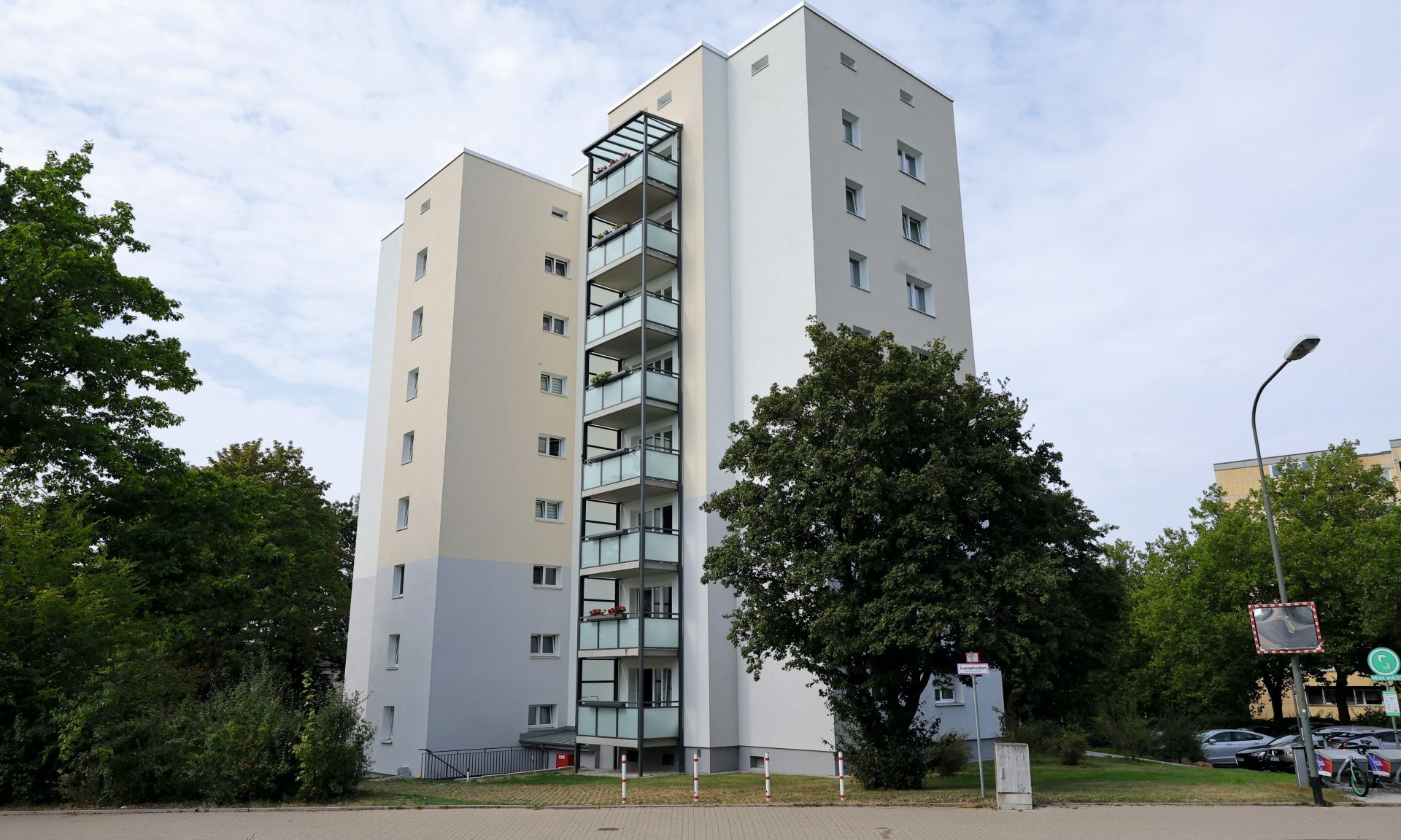 Blick auf ein modernisiertes Hochhaus, links und rechts davon stehen Bäume