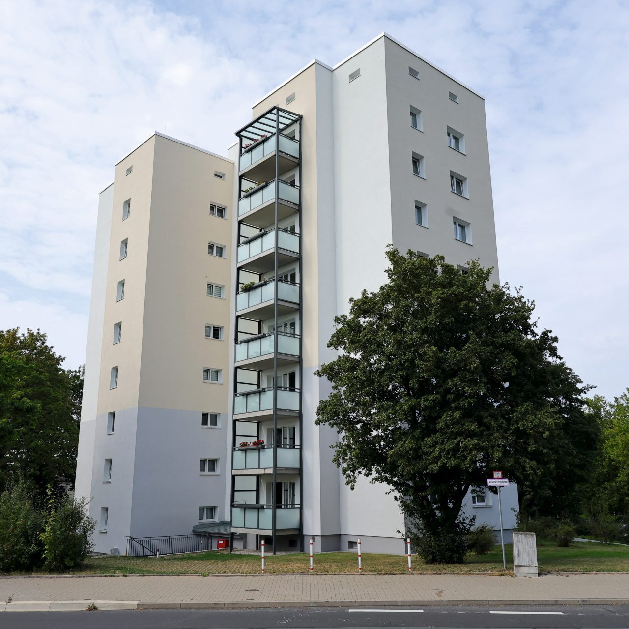 Blick auf ein modernisiertes Hochhaus, links und rechts davon stehen Bäume