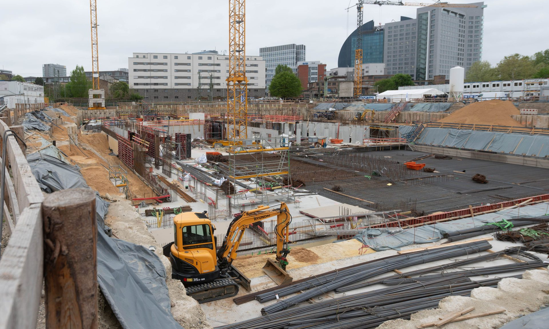 Blick auf eine Baustelle mit viel Baumaterial, Baufahrzeugen und Kränen.