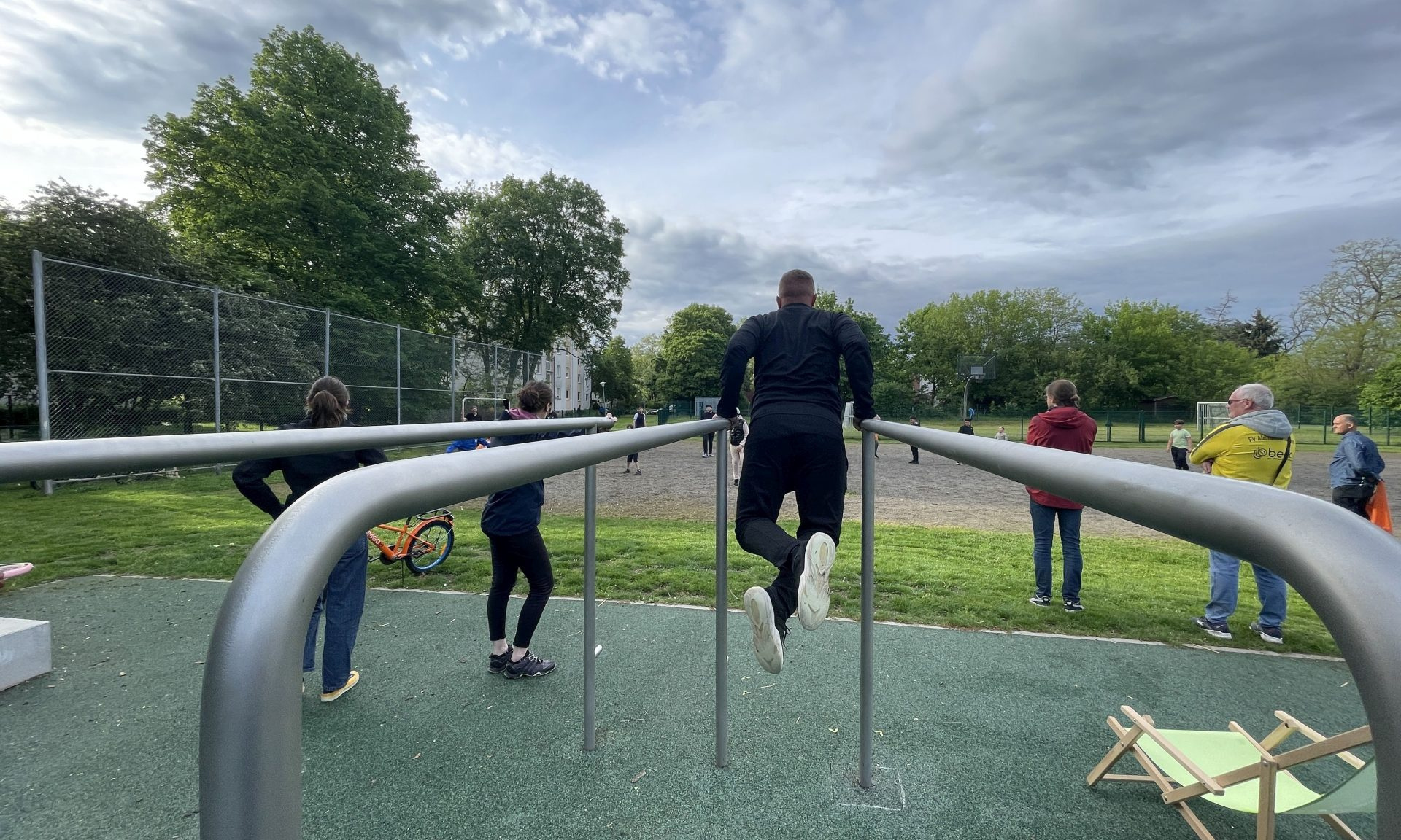 Sportgeräte in einer Parkanlage mit Menschen, die daran ihre Fitness trainieren