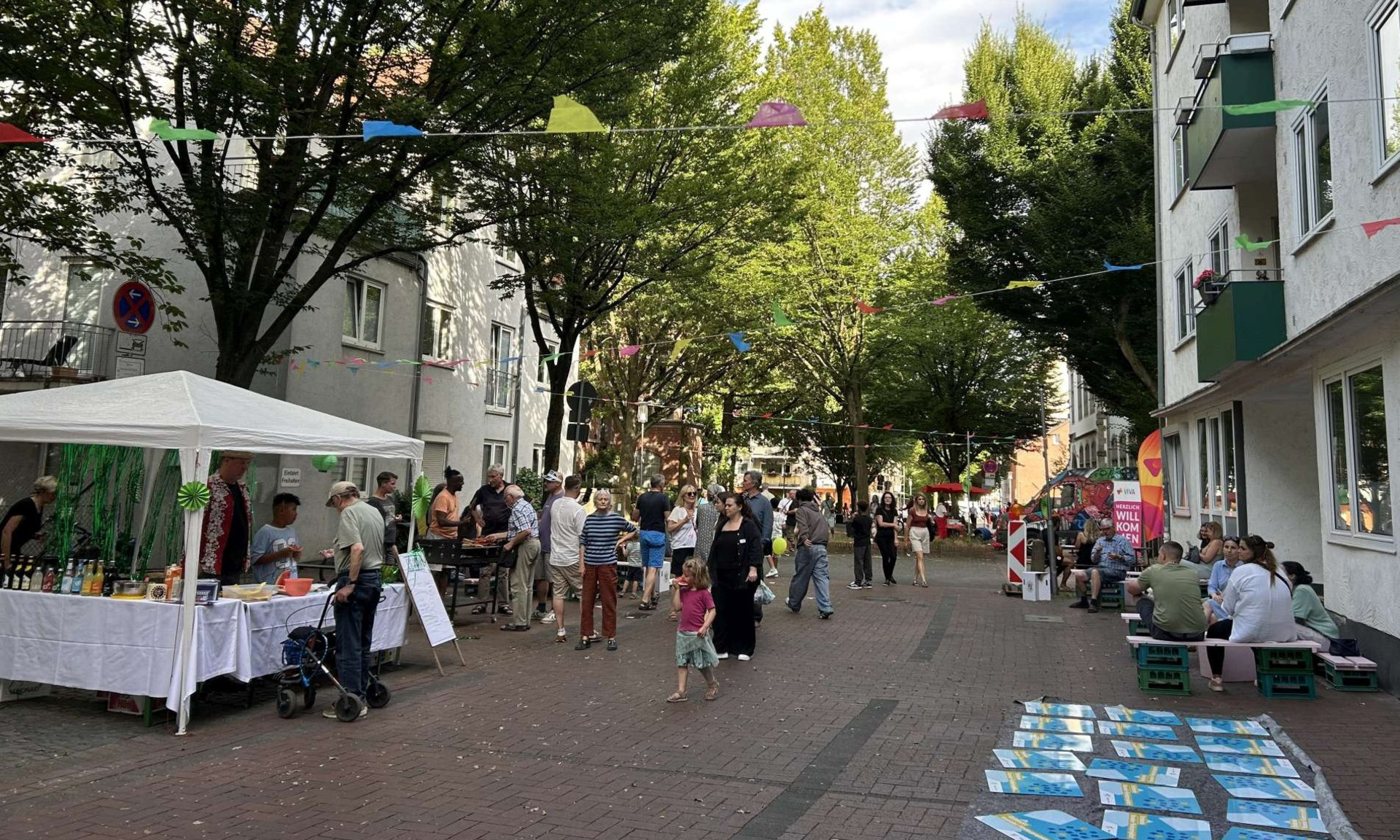 Mit Wimpeln geschmückte Straße, Menschen, die auf Bänken sitzen, vereinzelte Stände