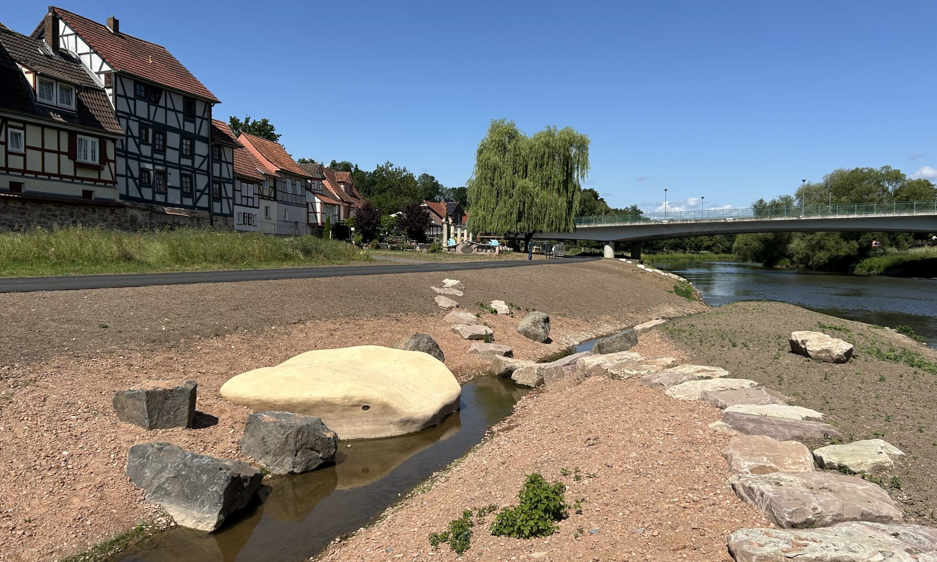 Freigelegter Altarm, Steine, die Fulda, Brücke im Hintergrund und Fachwerkhäuser