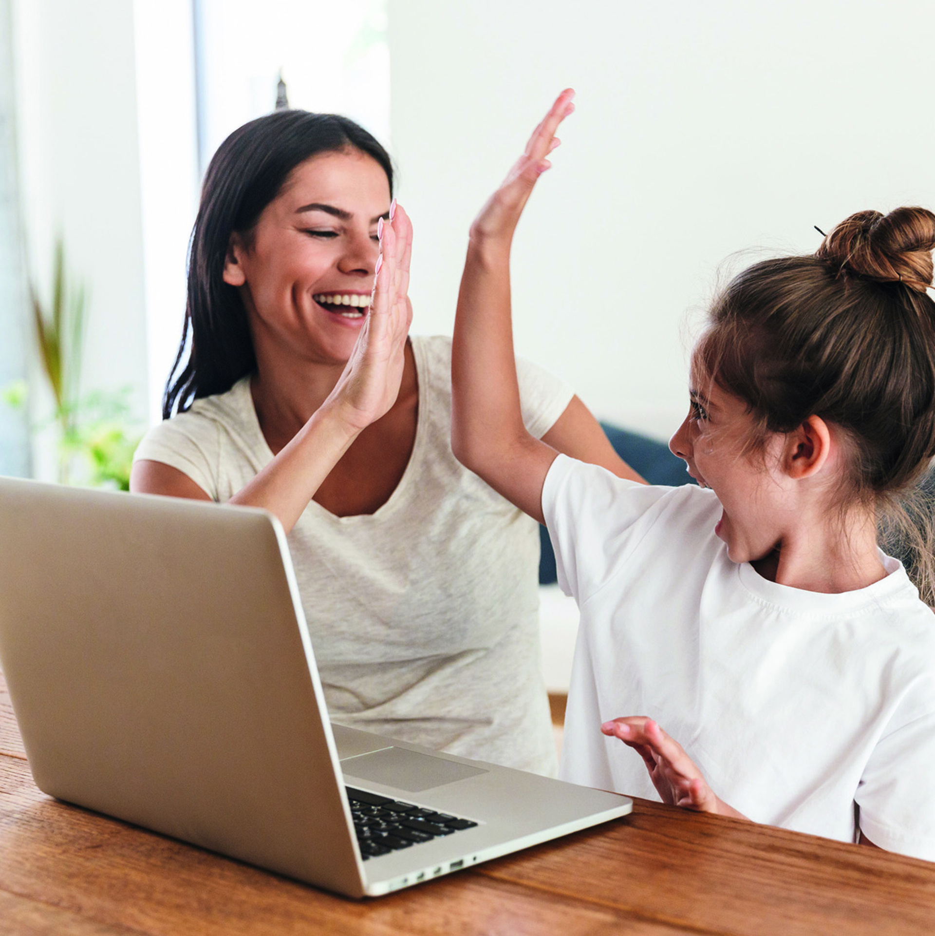 Frau und Kind sitzten vor einem Laptop und geben sich ein "High Five"
