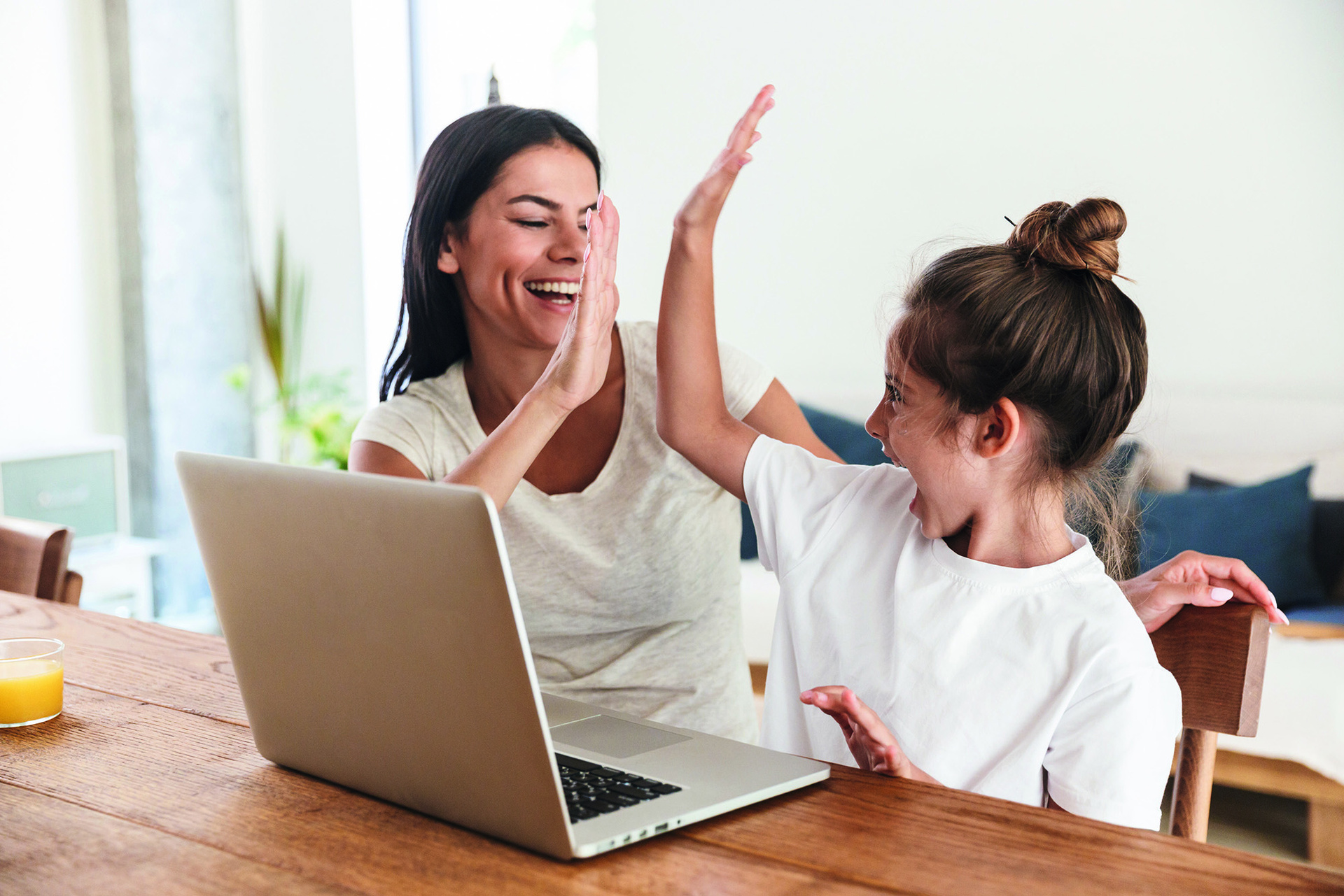 Frau und Kind sitzten vor einem Laptop und geben sich ein "High Five"