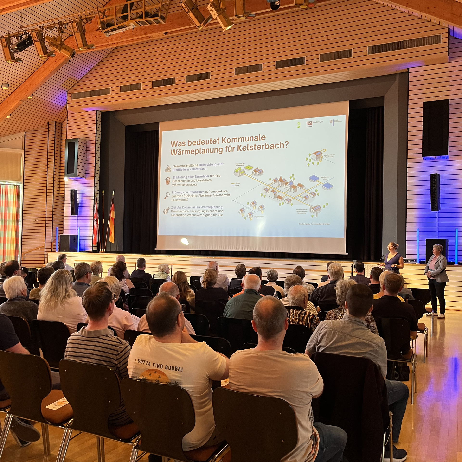 Die Bürger der Stadt Kelsterbach sitzen in einem Saal und schauen auf eine PowerPoint Präsentation.