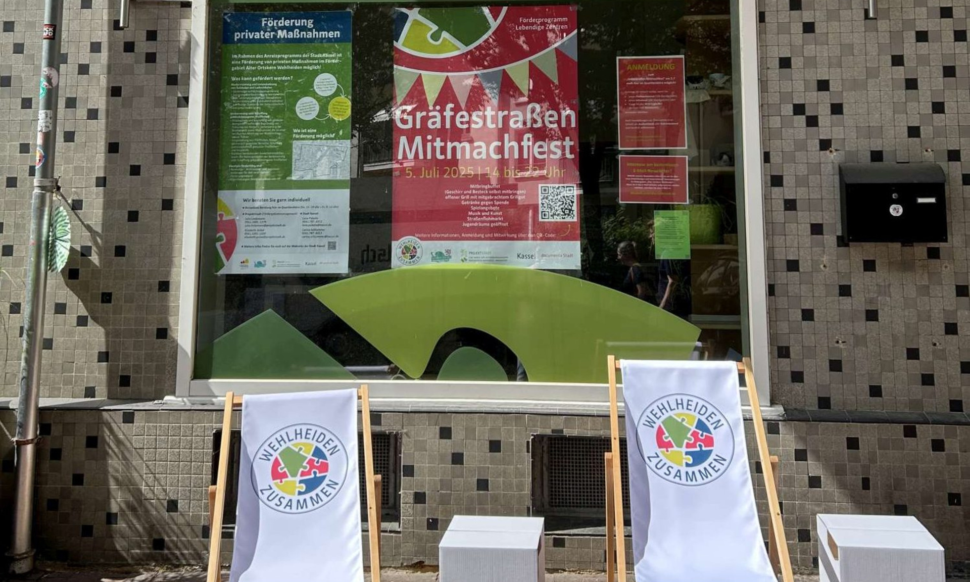 Das Quartiersbüro der ProjektStadt in Kassel-Wehlheiden. Im Fenster hängen viele Info-Zettel und Plakate, davor stehen Liegestühle