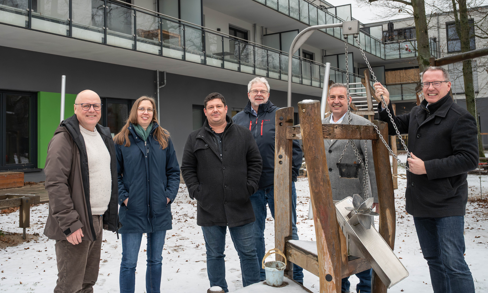 Sascha Holstein (2. v. re.), Leiter des Regionalcenters Kassel, und Servicecenterleiter Hendrik Hoekstra (3. v. re.) übergaben die Spende der NHW an den Vorstand der Lebenshilfe Gießen Dirk Oswald und den zuständigen Bereichsleiter Jan Hillgärtner. Spielgerät im Vordergrund, dahinter ein Gebäude, auf dem Boden Schnee