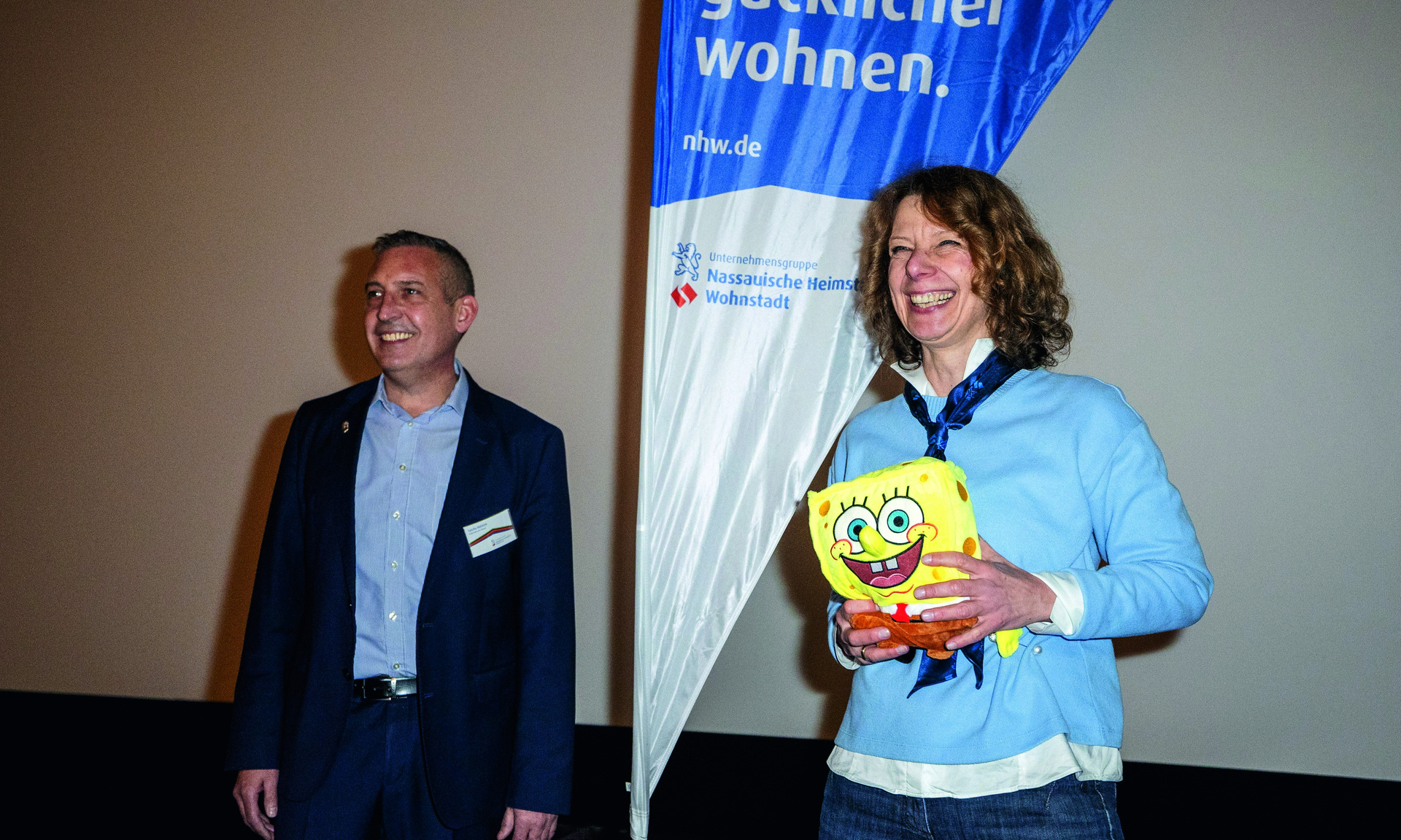 Das Bild zeigt Frau Linke aus der Sozialen Quartiersentwicklung der NHW mit NHW-Banner auf der Kinoveranstaltung