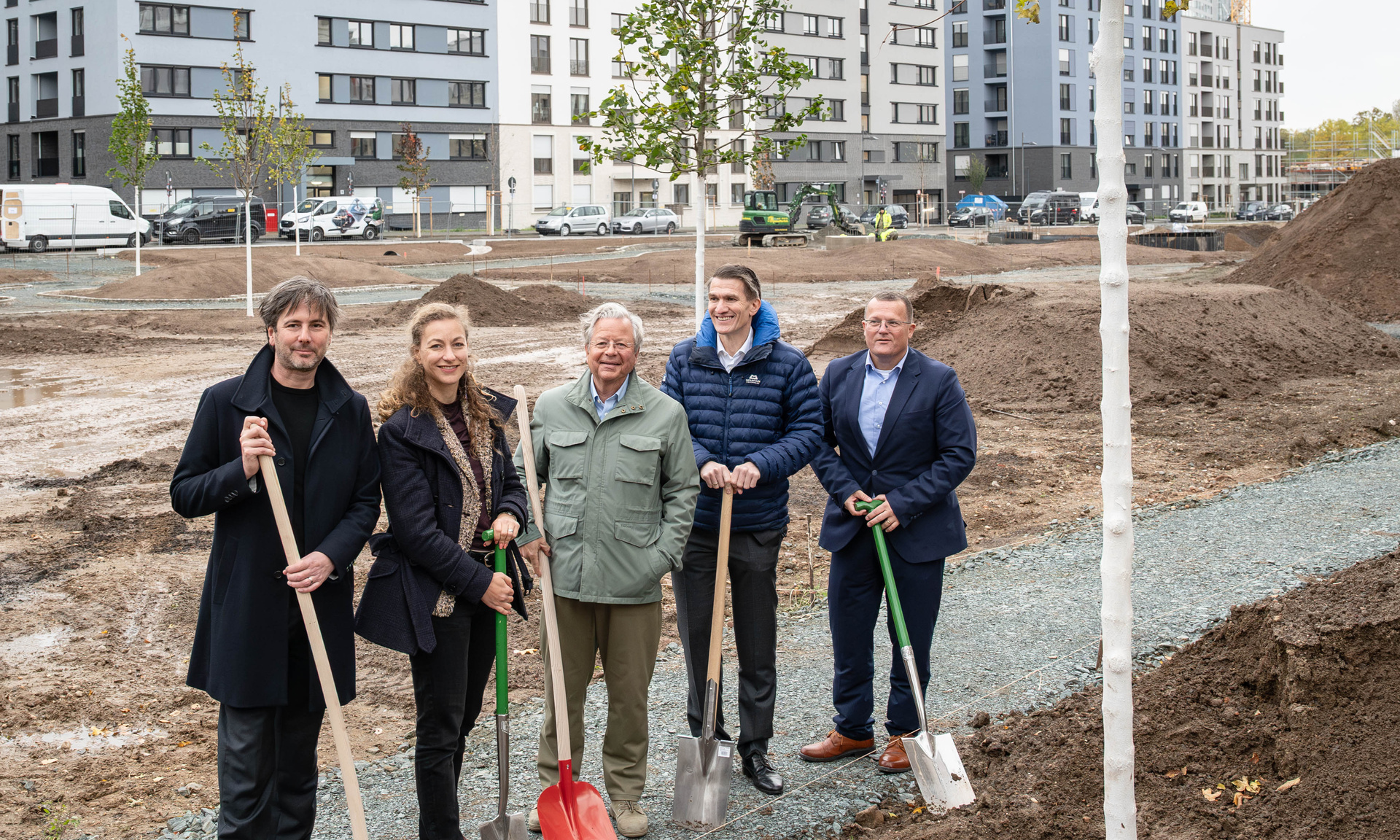 Fünf Personen mit Spaten in der Hand auf einer Baustelle im Querformat.