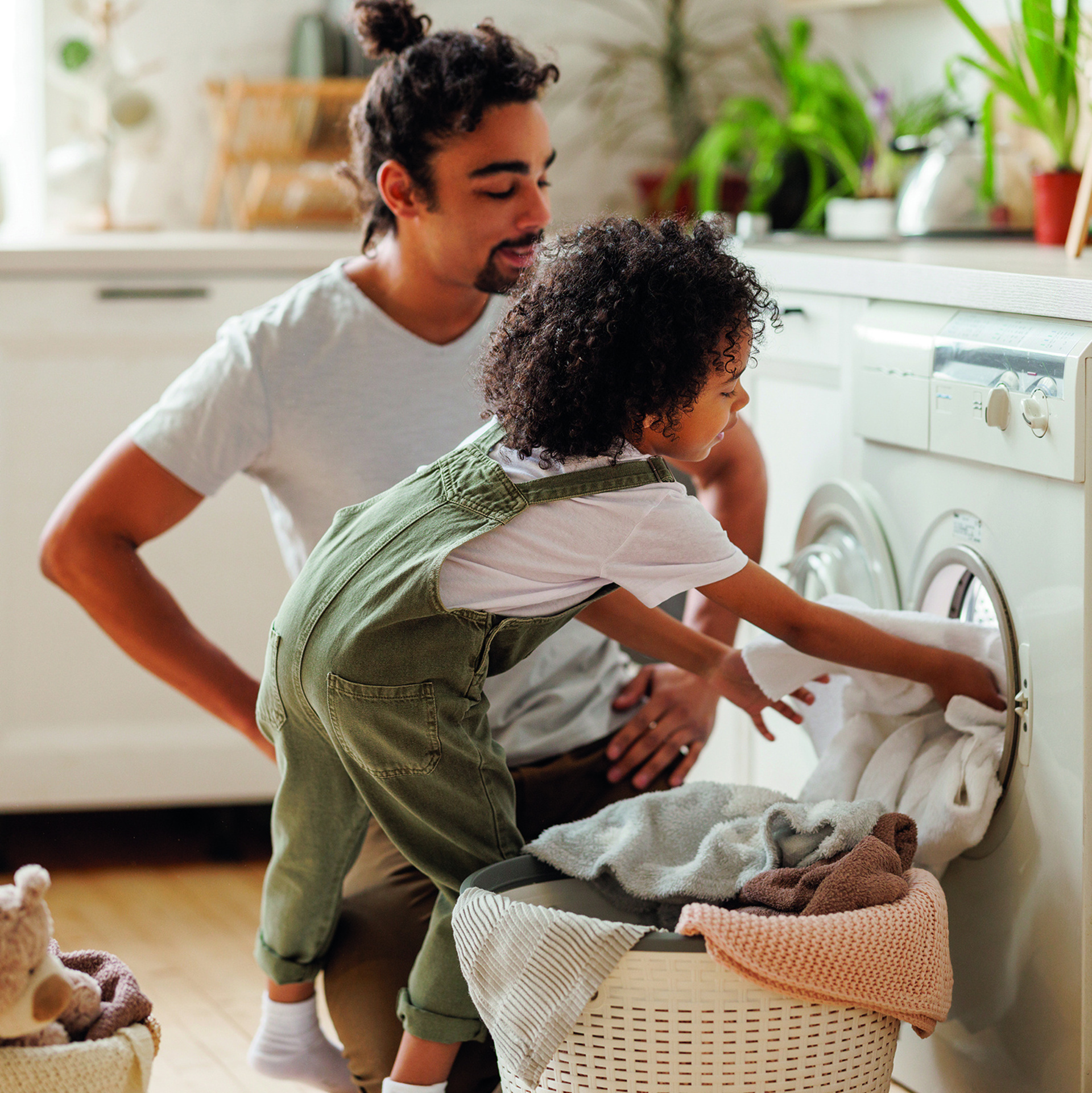 Ein Man und sein Kind räumen gemeinsam Wäsche in eine Waschmaschine.