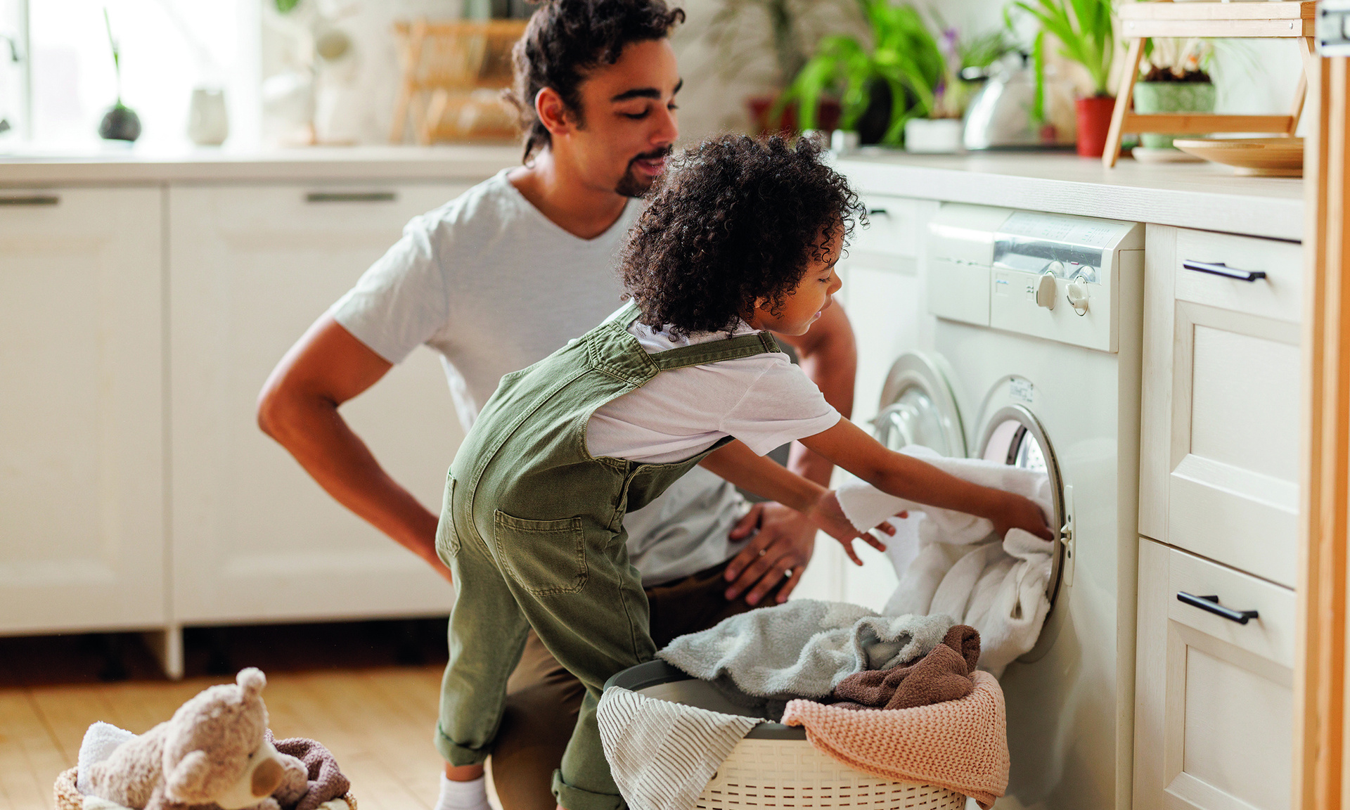 Ein Man und sein Kind räumen gemeinsam Wäsche in eine Waschmaschine.