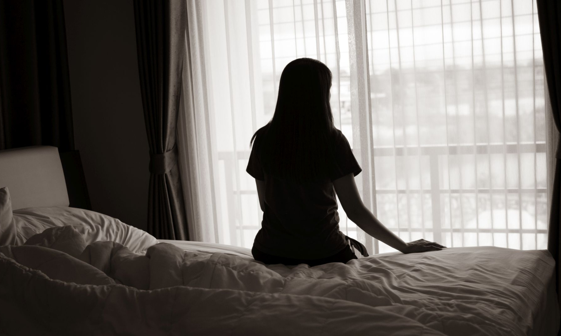 Frau von hinten auf Bett vor Fenster