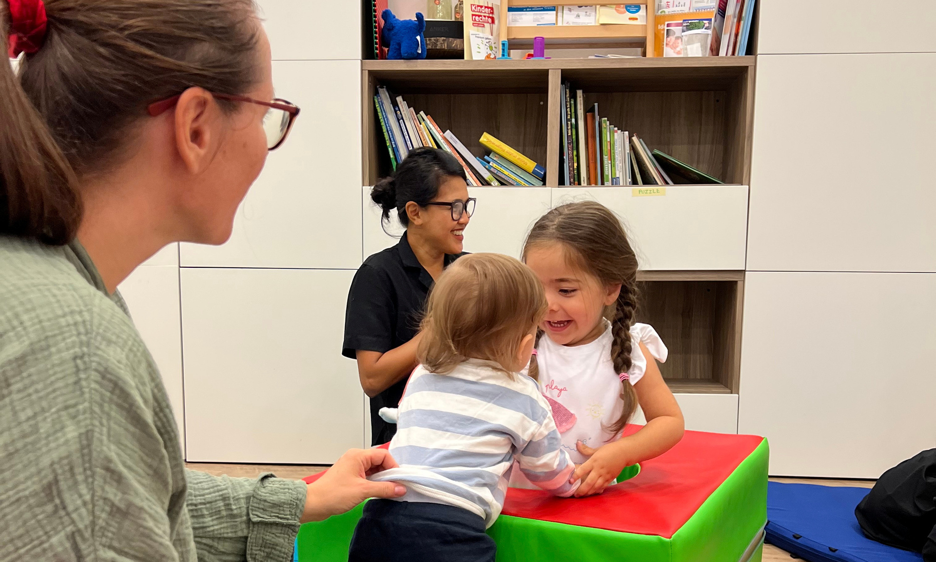 Zwei Kleinkinder die zusammen spielen. Mütter sind im Hintergrund