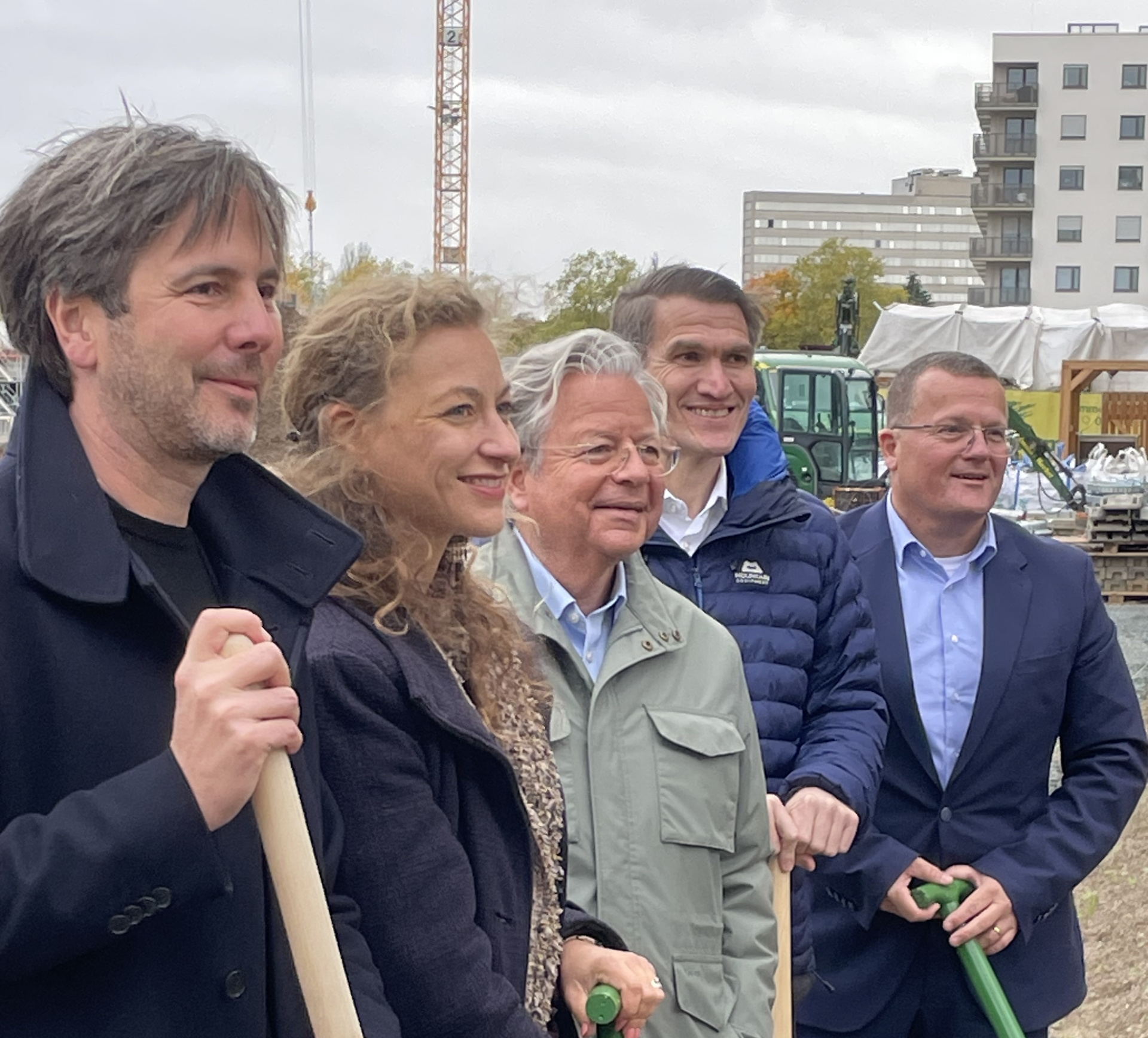 Fünf Personen mit Spaten in der Hand auf einer Baustelle im Hochformat