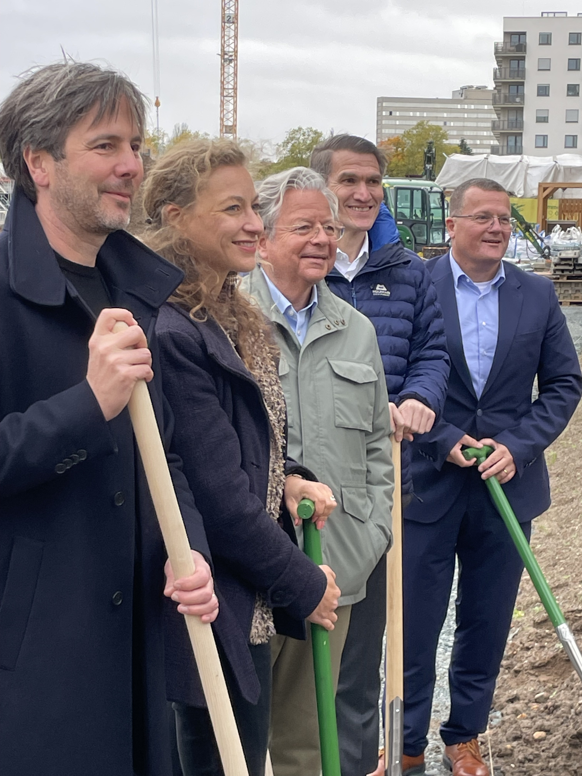 Fünf Personen mit Spaten in der Hand auf einer Baustelle im Hochformat