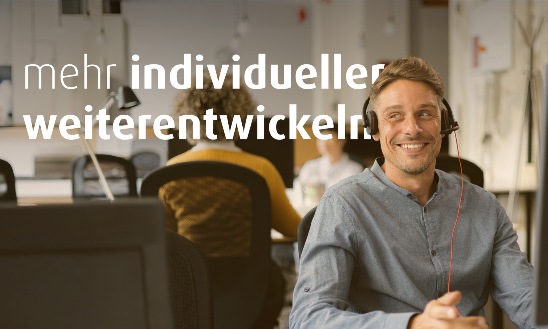 Ein Mann sitzt am Schreibtisch und hat ein Headset auf. Im Hintergrund sieht man weitere Personen an Schreibtischen. Auf dem Bild steht der Text "mehr individueller weiterentwickeln".