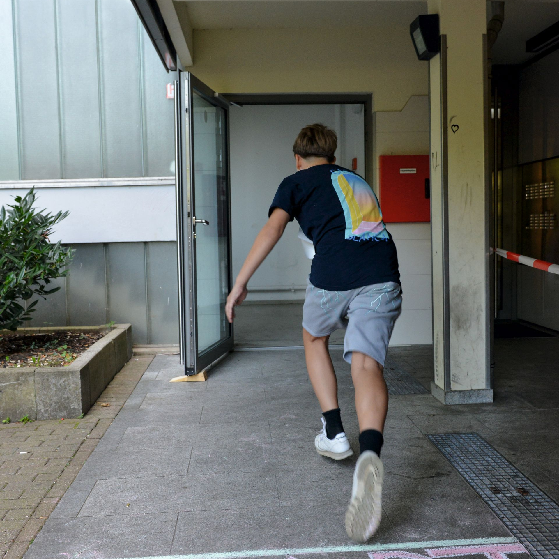 Auf dem Boden steht "Start" ein Junge rennt grade los in einen Hauseingang.