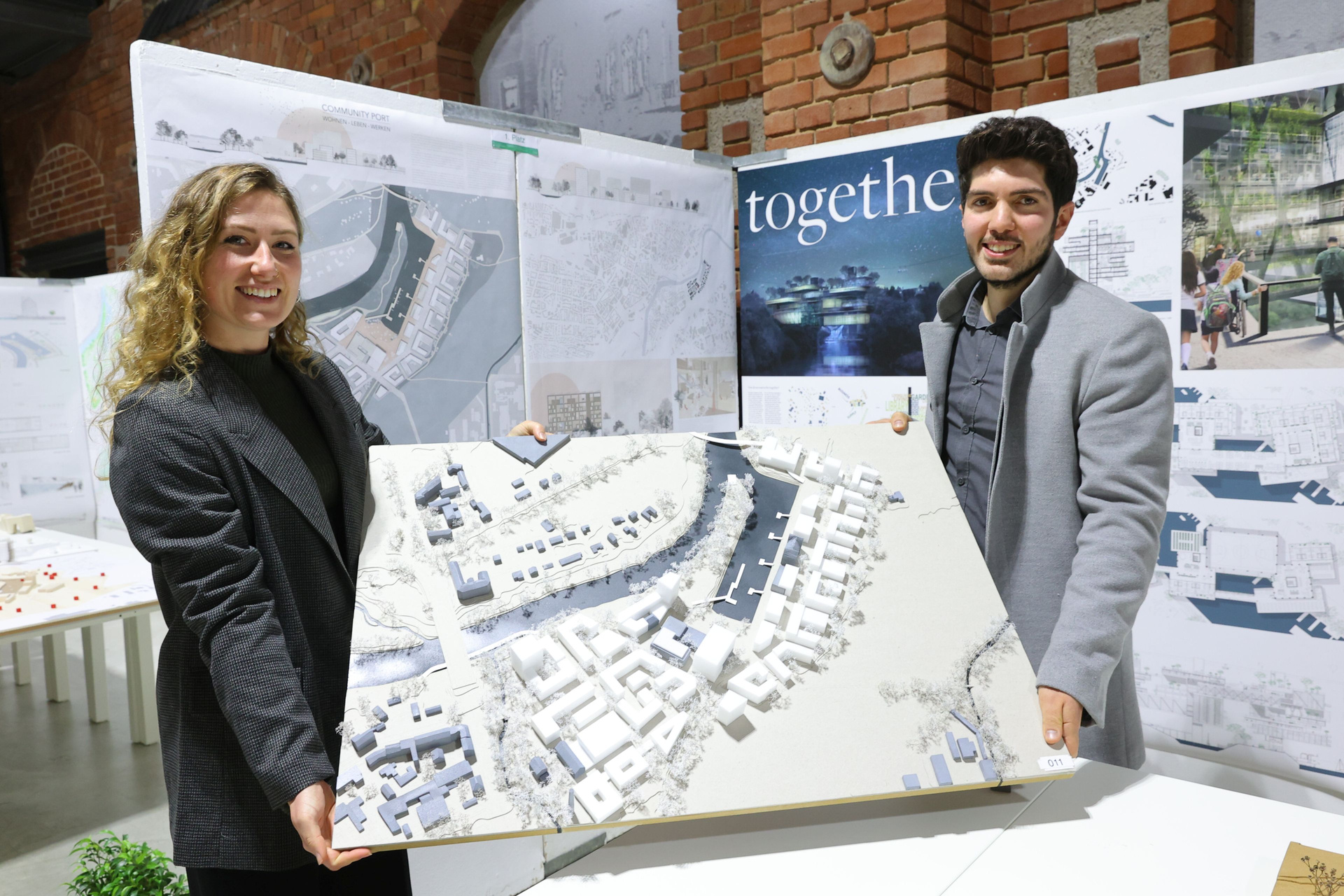 Melissa Krug und Necati Karalar halten ein Plakat mit ihrem Entwurf in der Hand