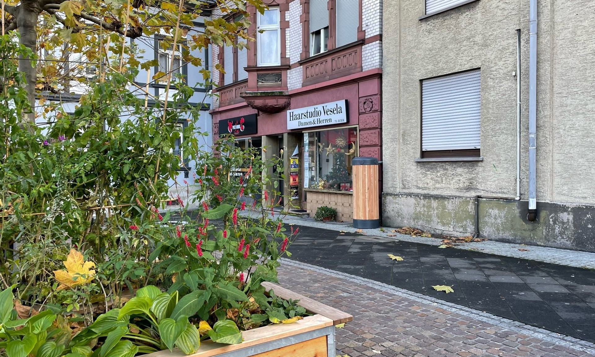 Pflanzbeet im Vordergrund, Regentonne an Hauswand im Hintergrund