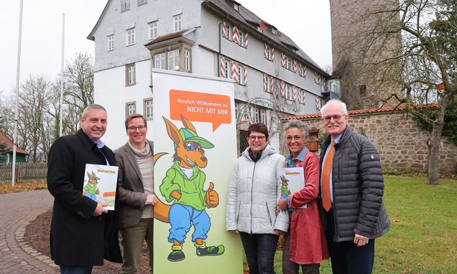 Fünf Personen mit einem Plakat zwischen ihnen stehen vor einem mittelalterlich anmutenden Gebäude:(v. li.) Sascha Holstein (NHW-Regionalcenterleiter Kassel) übergibt die Weihnachtsspende der NHW für Nordhessen an Heide Aust (Geschäftsführerin), Anita Hofmann (Vorstand), Kerstin Jung (Schatzmeisterin) und Max Ostrowski (2. Vorsitzender) vom Verein Schule machen ohne Gewalt.