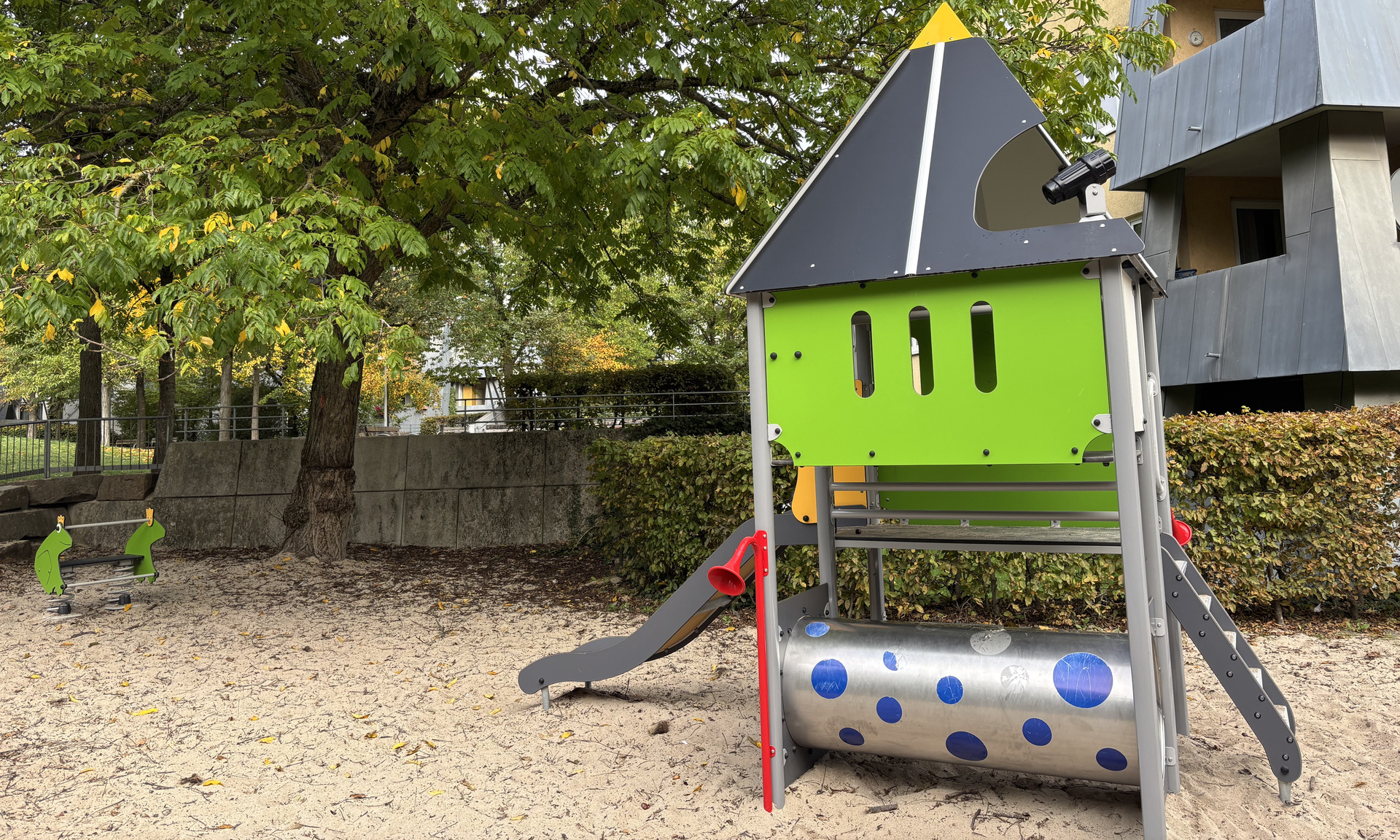 Grünes Spielplatzelement mit Spitzdach, Rutsche, Kletterleiter und Röhre