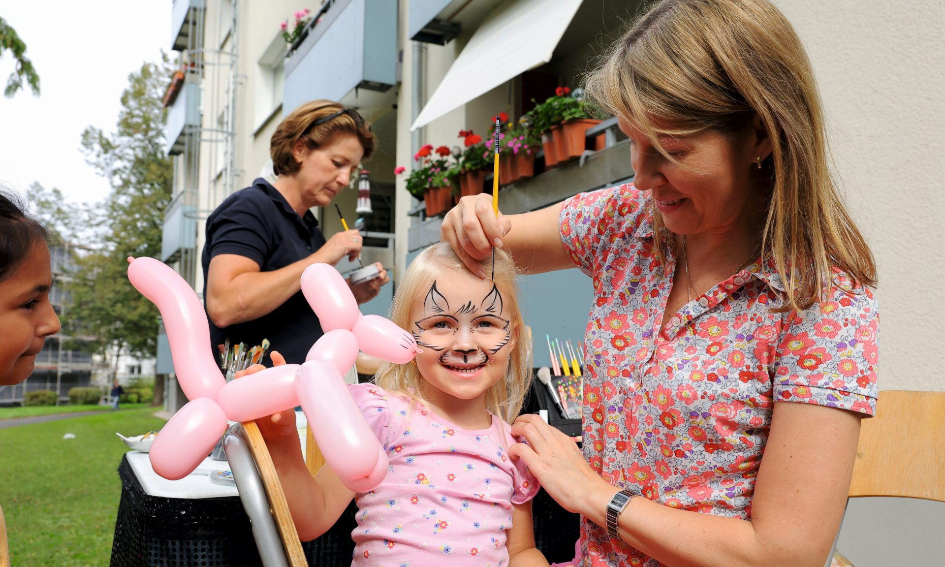 Ein Kind beim Kinderschminken, im Hintergrund ein Mehrfamilienhaus