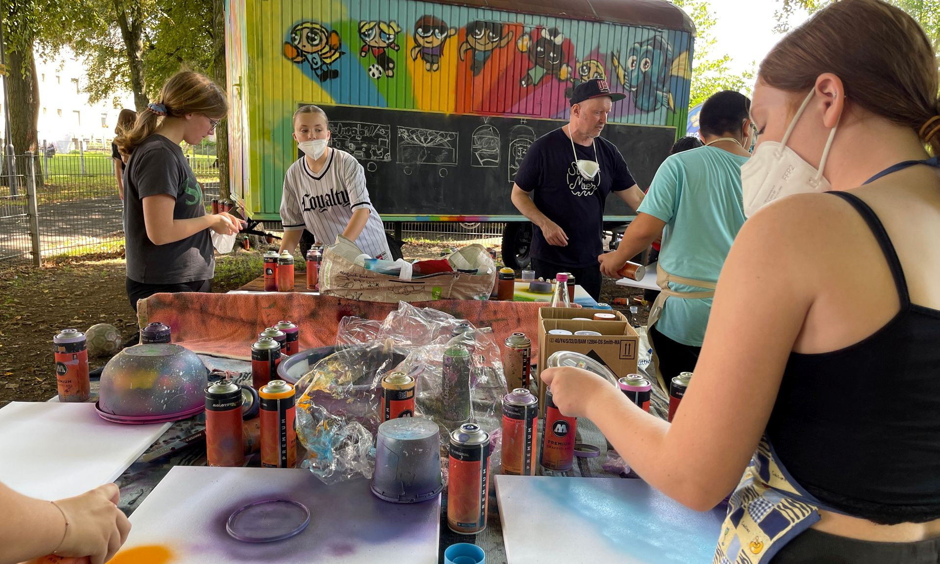 Kinder gestalten beim Kreativworkshop mit Sprühdosen den Bauwagen des Spielmobils