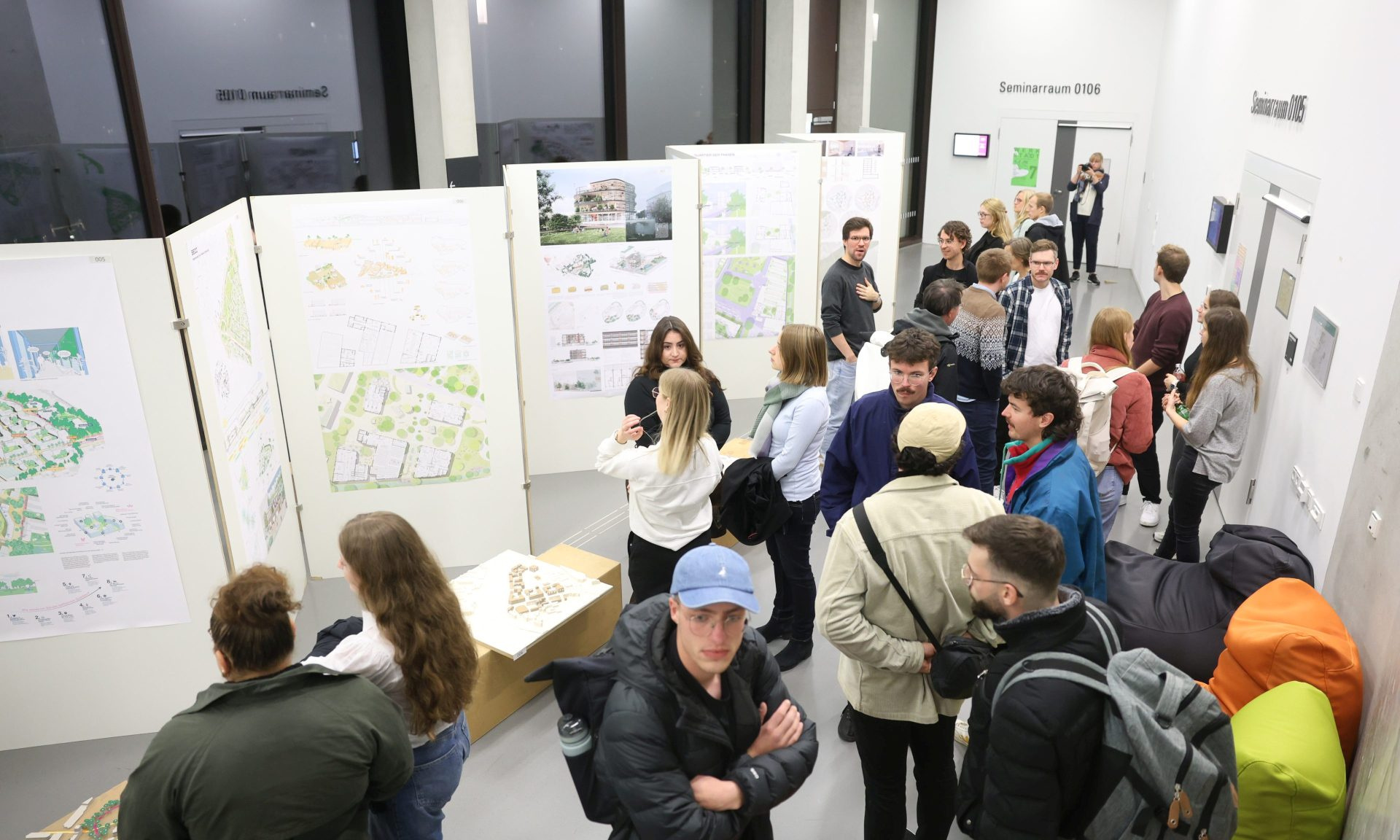 Blick von oben auf eine Gruppe von Menschen, die sich die Ausstellung der Wettbewerbsentwürfe ansieht.