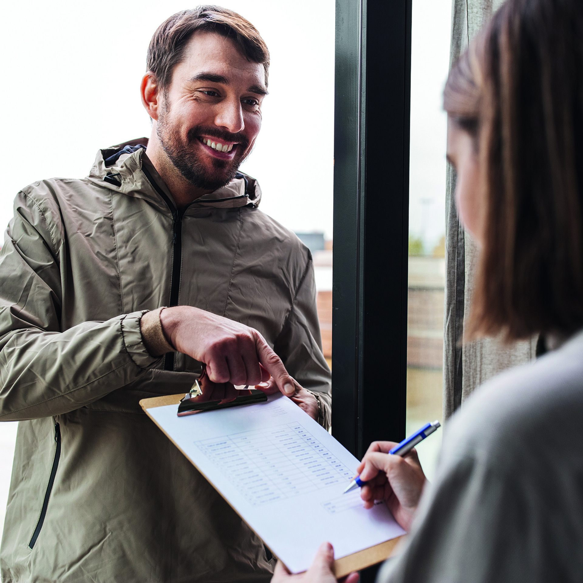 Ein Mann an der Haustür zeigt einer älteren Dame einen Vertrag in Papierform und wo sie unterzeichnen muss.