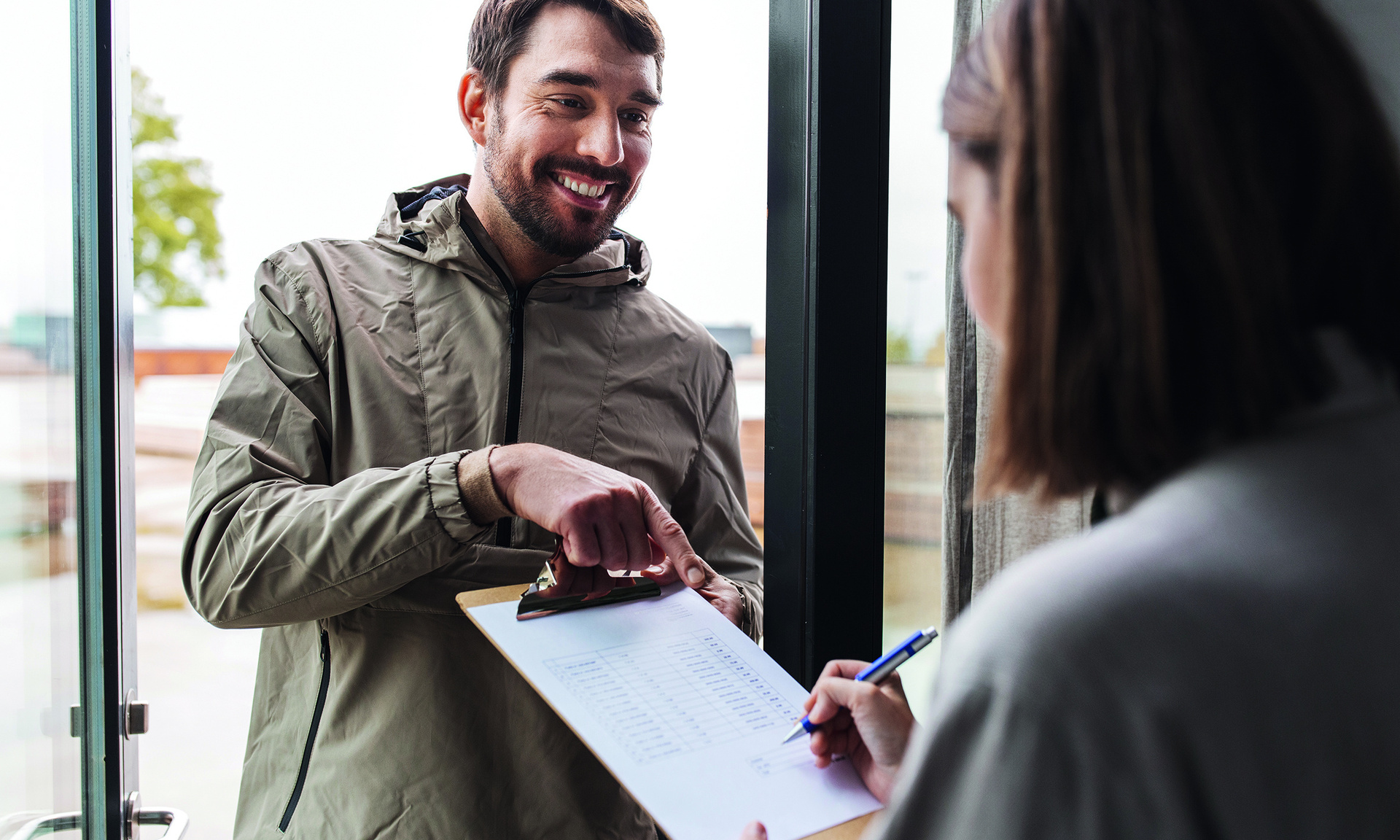 Ein Mann an der Haustür zeigt einer älteren Dame einen Vertrag in Papierform und wo sie unterzeichnen muss.