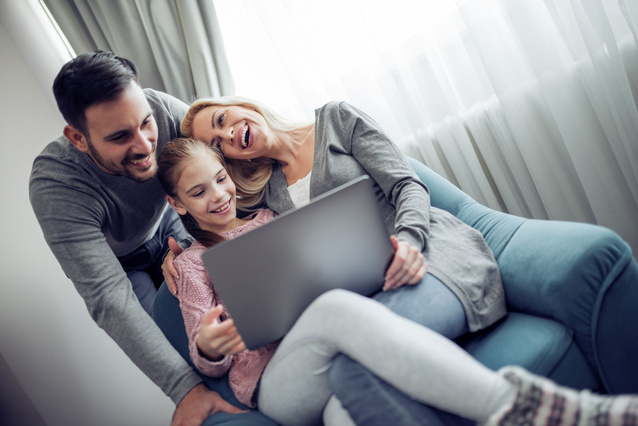 Mann, Frau und Mädchen sitzen auf dem Sofa und schauen auf einen Bildschirm.