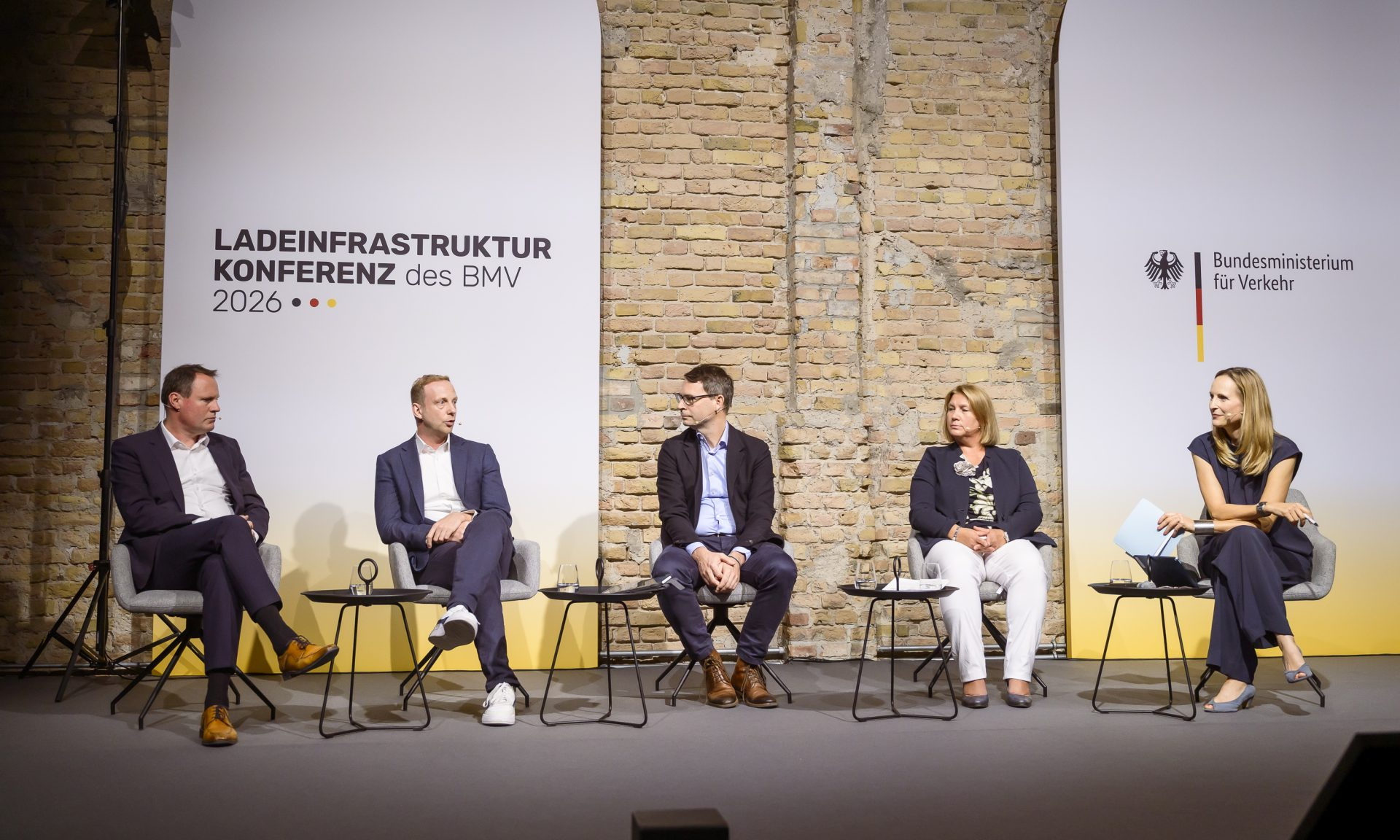 Drei Männer und zwei Frauen beim Gespräch auf einem Podium, im Hintergrund der Schriftzug "Ladeinfrastrukturkonferenz"