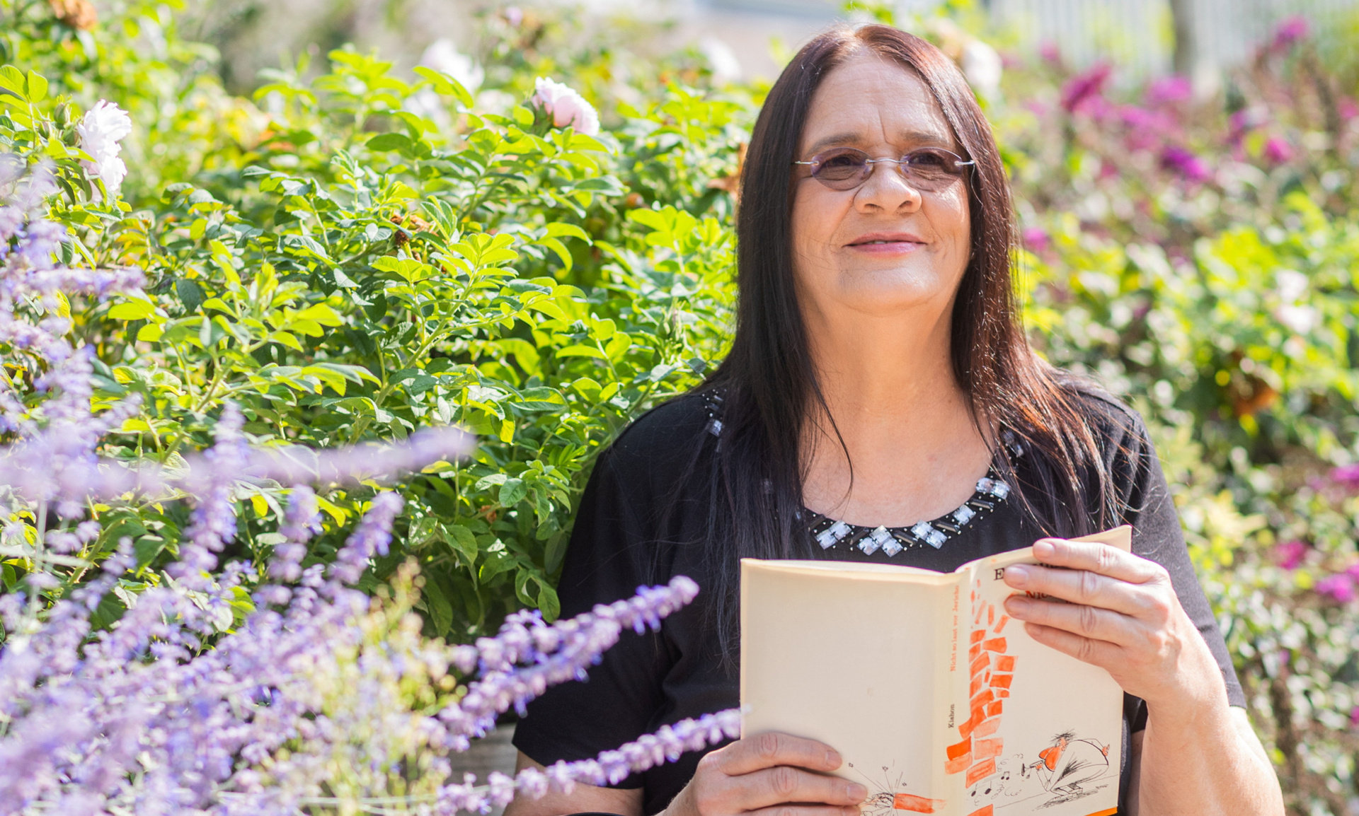 Mieterin sitzt auf einer Bank und liest in einem Buch. Hinter ihr sind Blumen zu sehen.