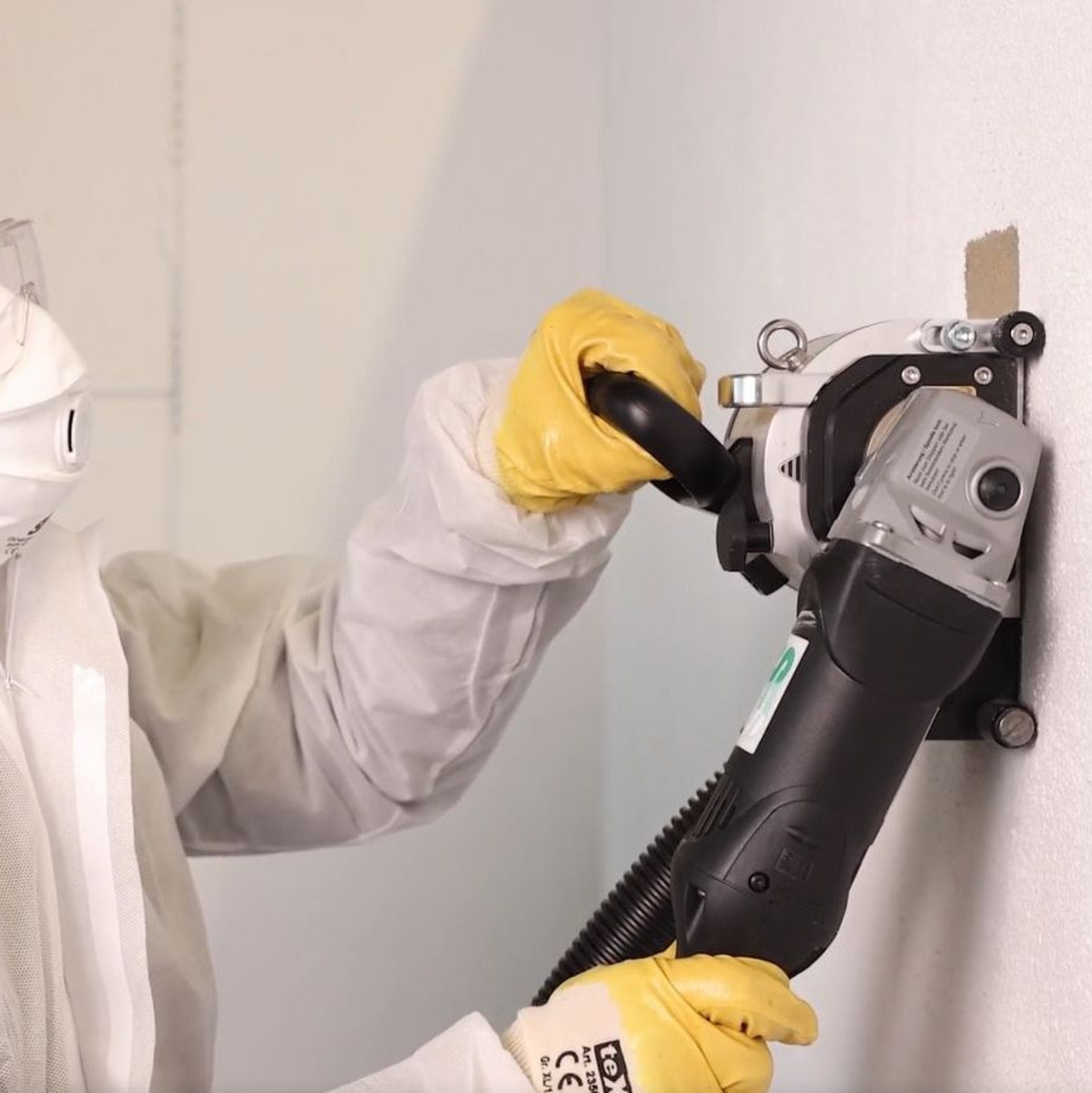 Mann in Schutzanzug entfernt maschinell Asbest von der Wand.