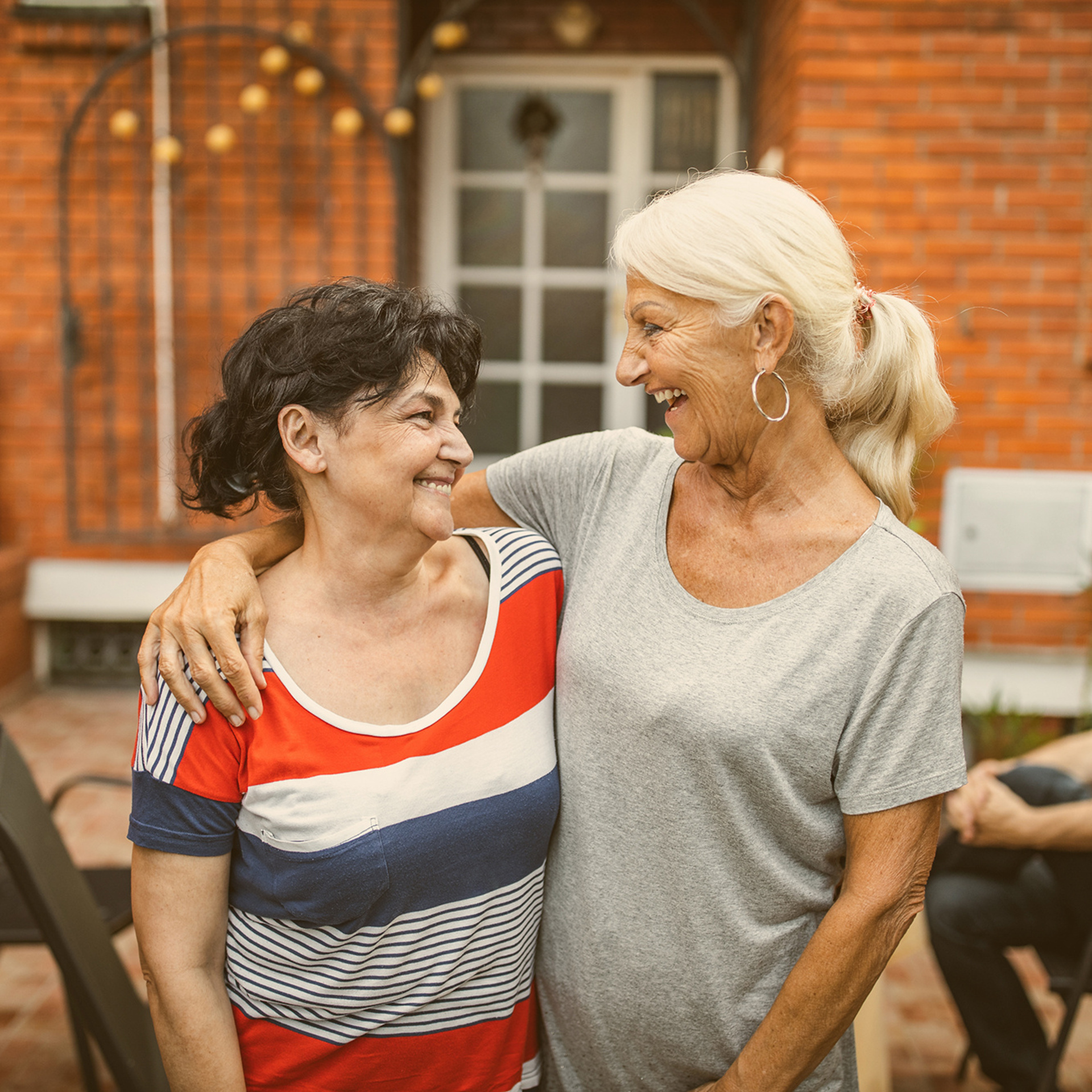Zwei ältere Frauen halten sich seitlich im Arm und lachen sich an.