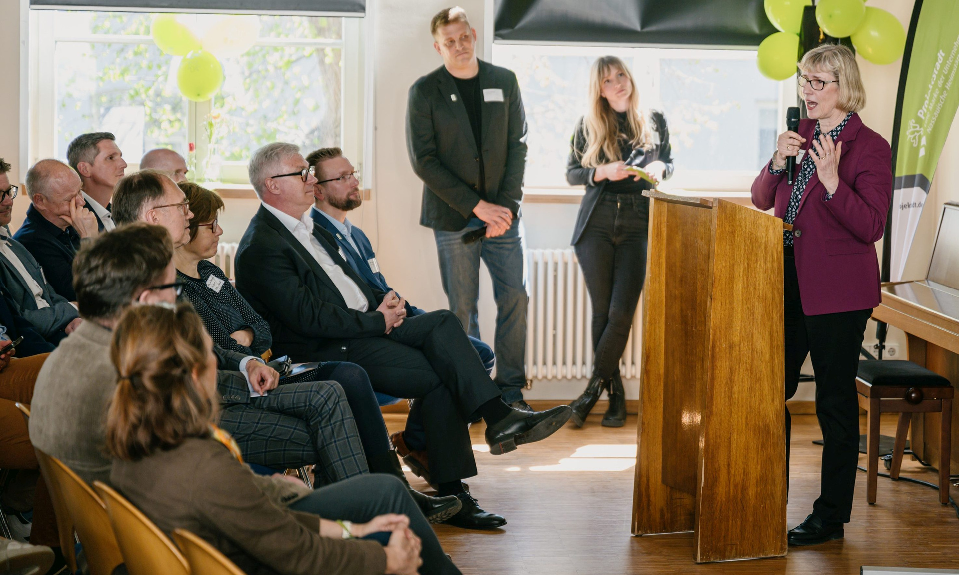 Rechts NHW-Geschäftsführerin Monika Fontaine-Kretschmer mit Mikrofon und Mischpult, links die ersten Reihen des Publikums.