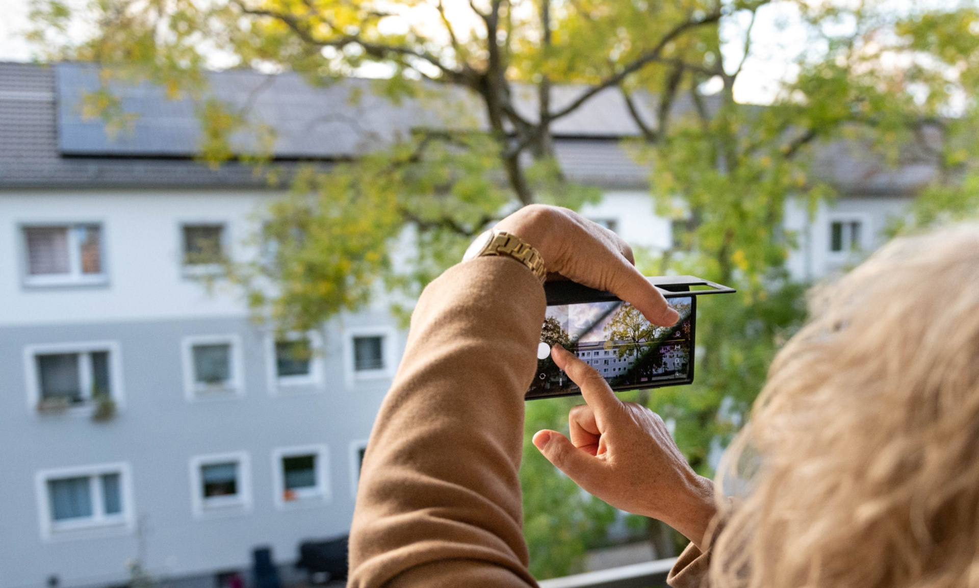 Frau macht Handyfoto von Dach mit Photovoltaik