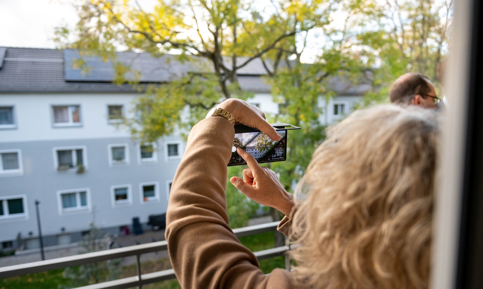 Frau macht Handyfoto von Dach mit Photovoltaik